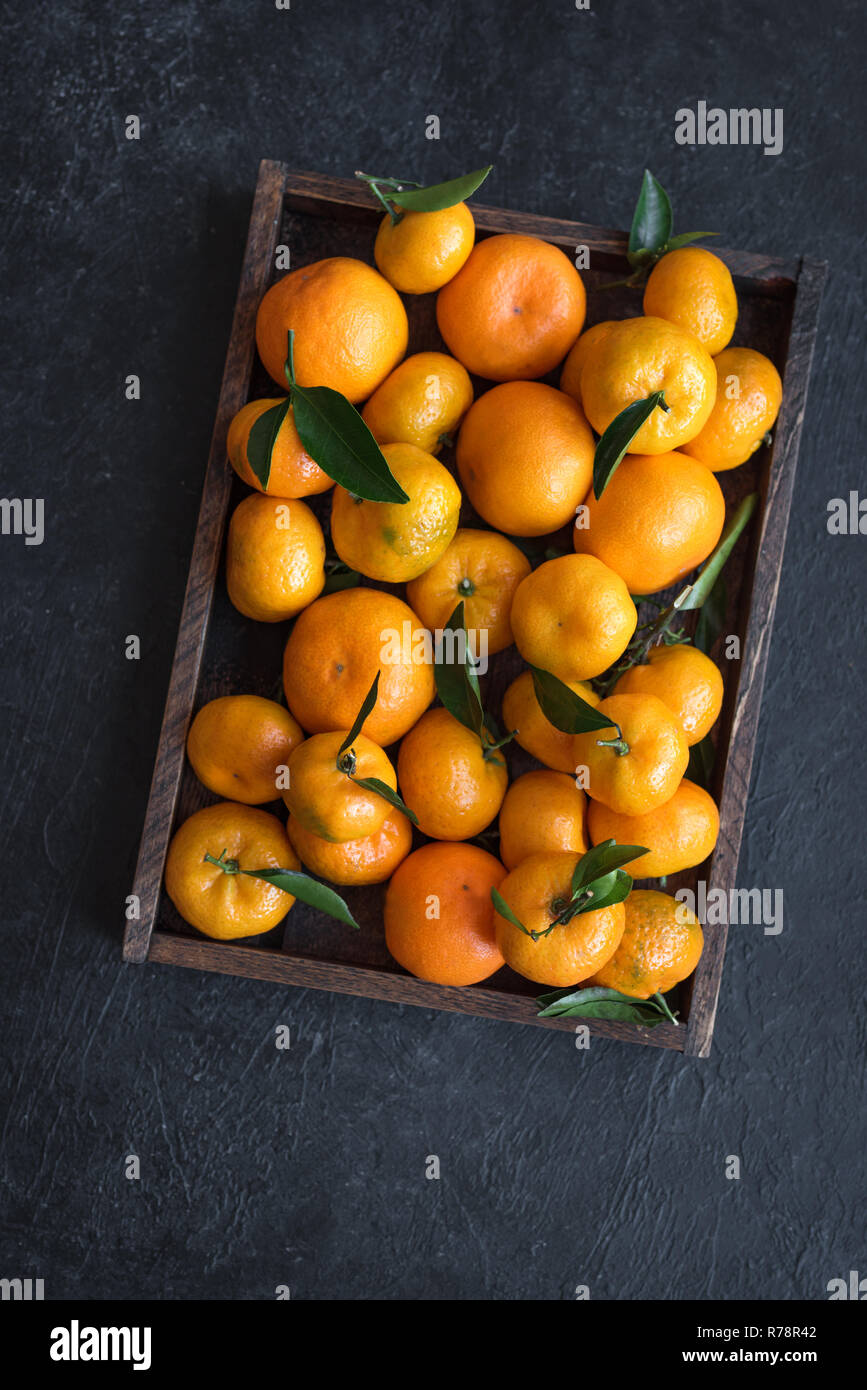 Tangerini (arance, clementine, agrumi) con foglie verdi nella casella su sfondo nero, copia dello spazio. Foto Stock