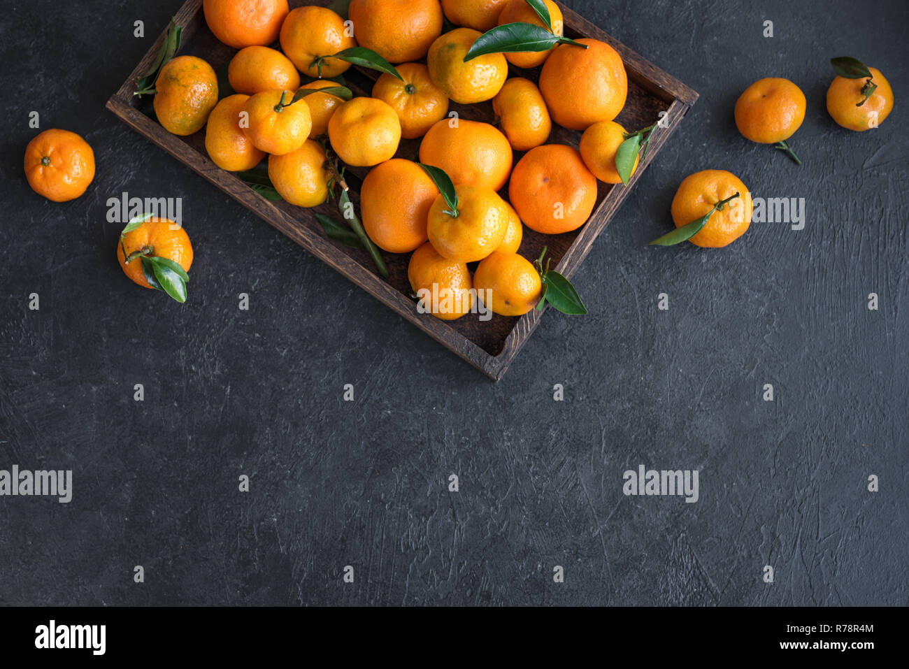 Tangerini (arance, clementine, agrumi) con foglie verdi nella casella su sfondo nero, copia dello spazio. Foto Stock