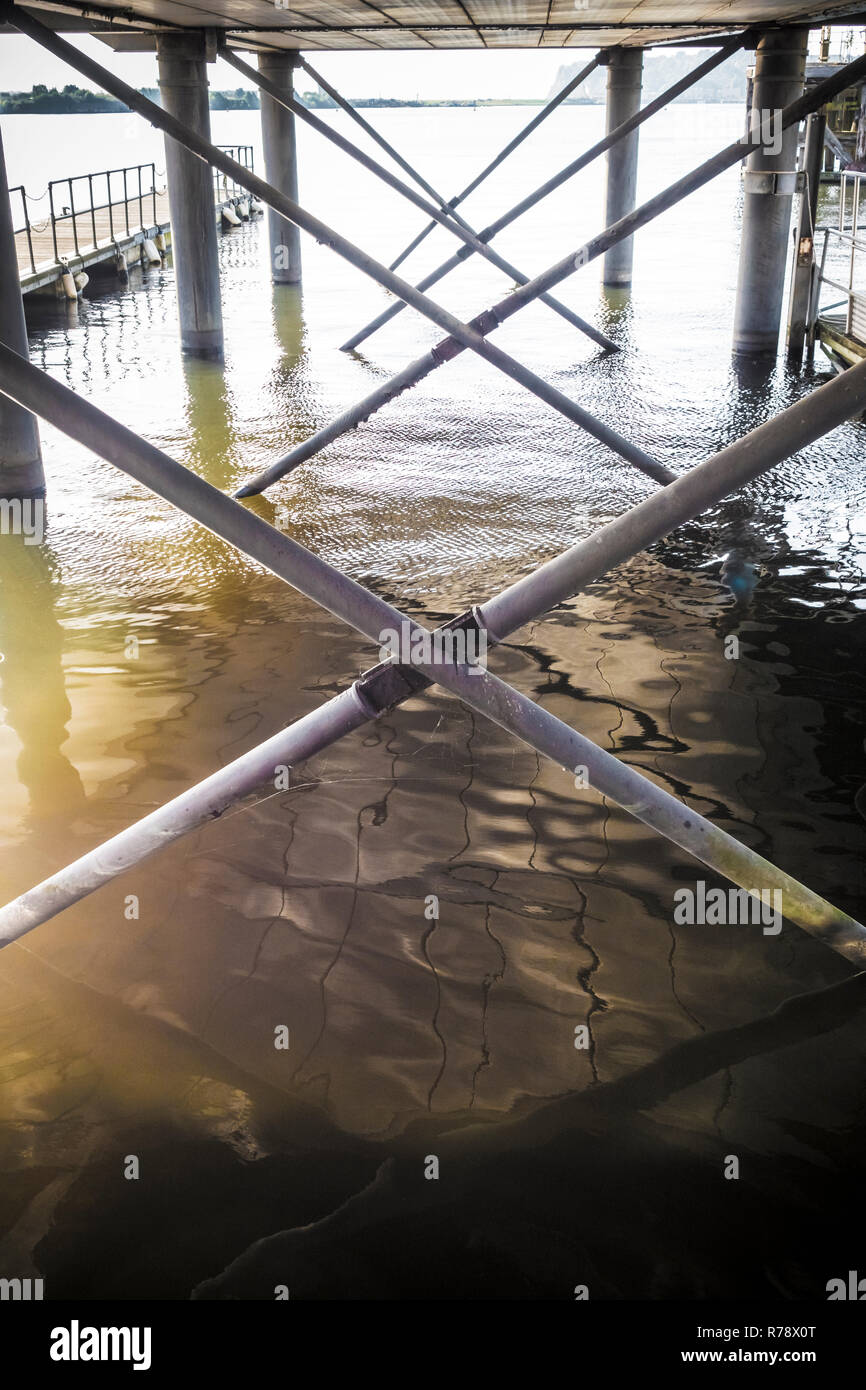 Vista sinistri di acqua increspata sotto un dock sollevata o boardwalk con riflessi della struttura di supporto. La Baia di Cardiff, Galles , REGNO UNITO Foto Stock