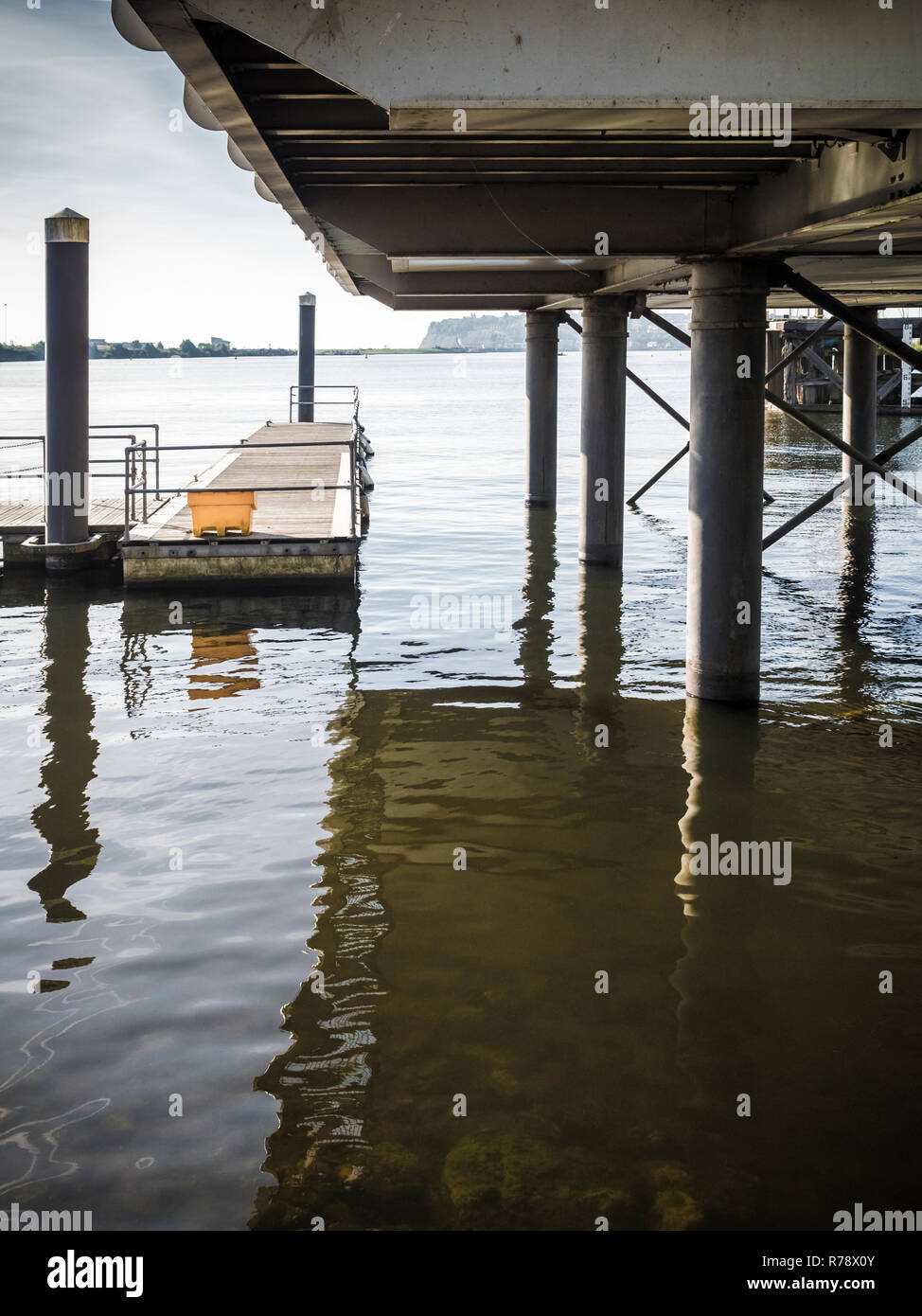 Vista sinistri di acqua increspata sotto un dock sollevata o boardwalk con riflessi della struttura di supporto. La Baia di Cardiff, Galles , REGNO UNITO Foto Stock