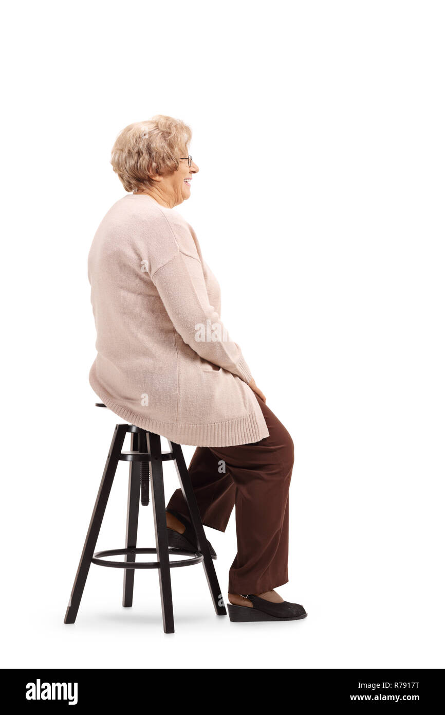 A piena lunghezza shot di un senior donna seduta su una sedia sgabello e posa isolati su sfondo bianco Foto Stock