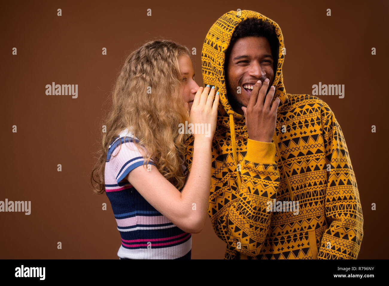 Ragazza adolescente whispering a felice l'uomo africano che è ridere Foto Stock