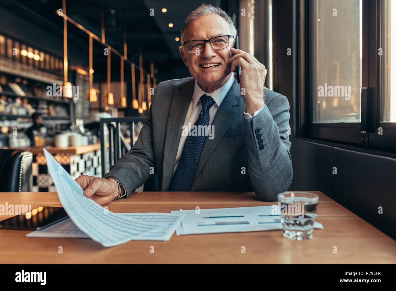 Sorridente imprenditori maturi udienza presso la caffetteria di parlare al telefono con il documento in mano. Felici gli imprenditori senior rendendo un telefono al cliente. Foto Stock