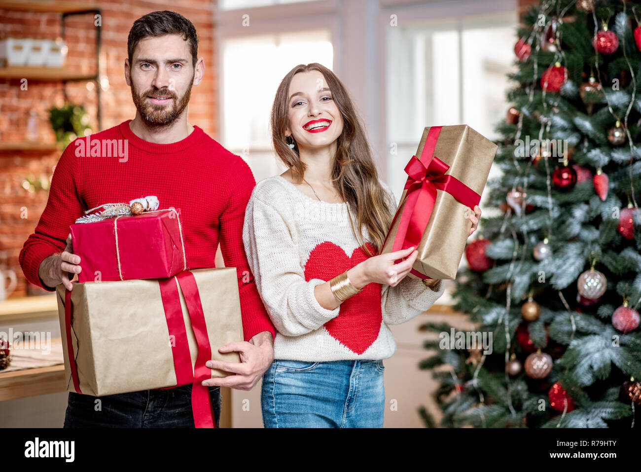 Ritratto di una giovane coppia adorabile in maglioni in piedi insieme con  il nuovo anno doni vicino all'albero di Natale a casa Foto stock - Alamy