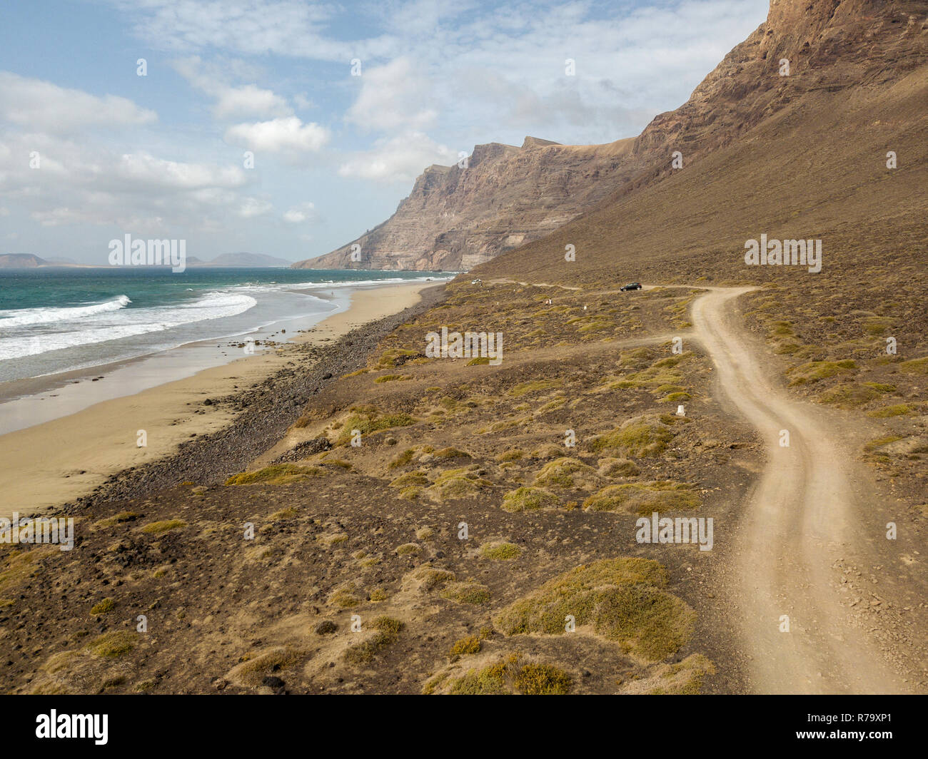 Vista aerea della spiaggia di Famara, Lanzarote, Isole Canarie, Spagna. Risco di Famara, rilievo, montagne che si affacciano sull'Oceano Atlantico. Strada sterrata Foto Stock