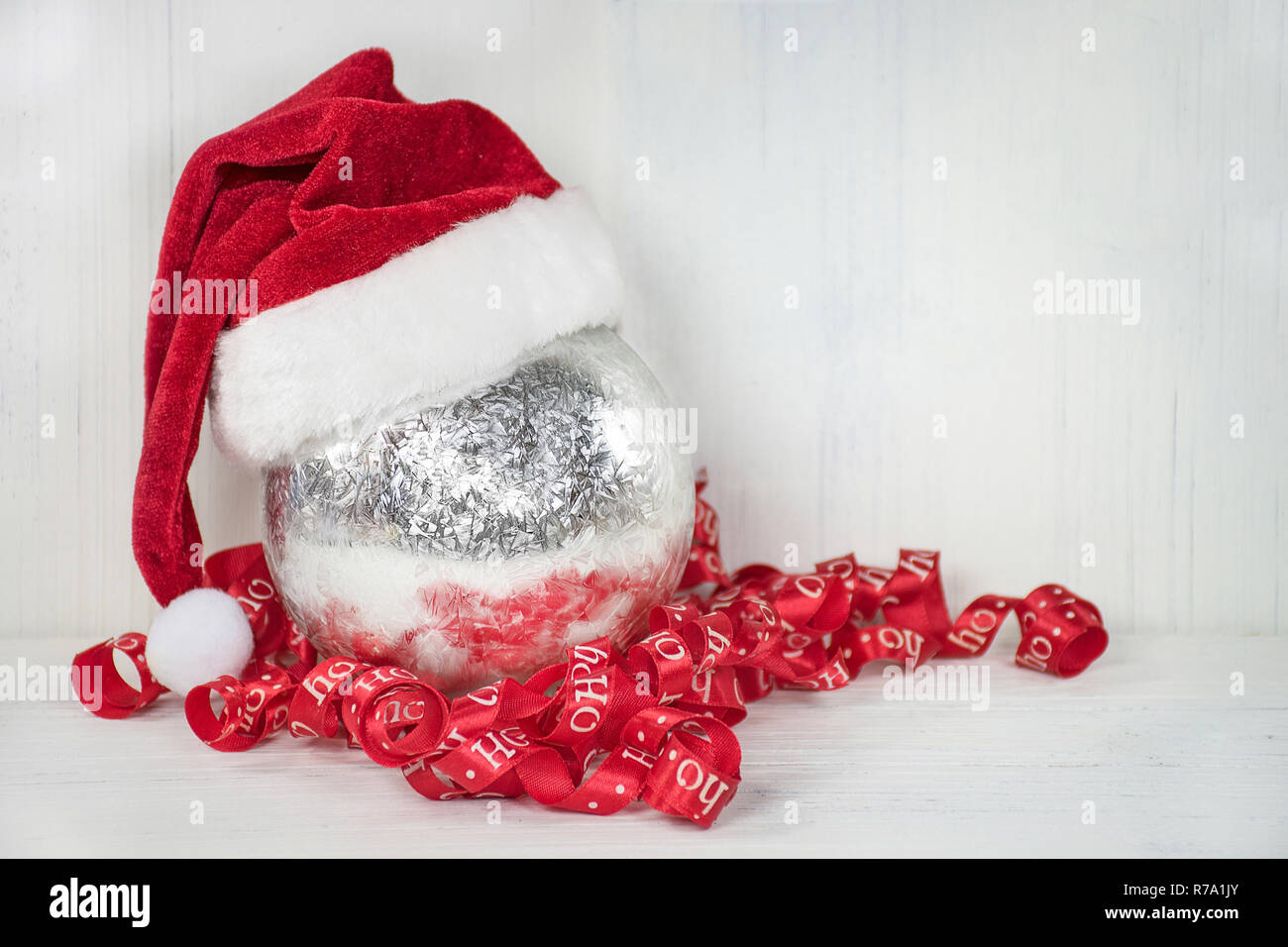 Santa Claus hat sull'argento ornamento di Natale con red curly vacanza sul nastro di legno dipinto di bianco Foto Stock