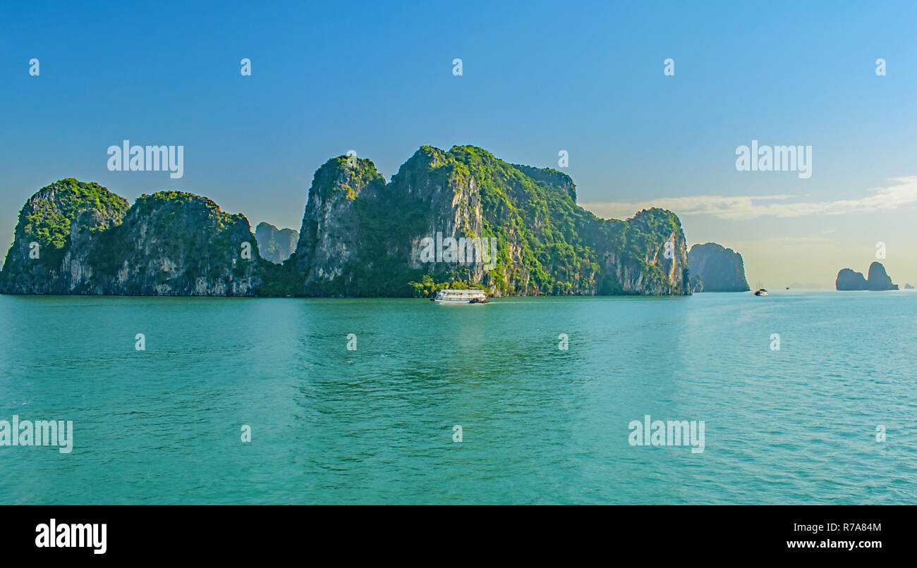 Le imbarcazioni turistiche vela il passato loming pietre calcaree carsiche in blu tranquilla baia di Halong, Vietnam Novembre 2018 Foto Stock