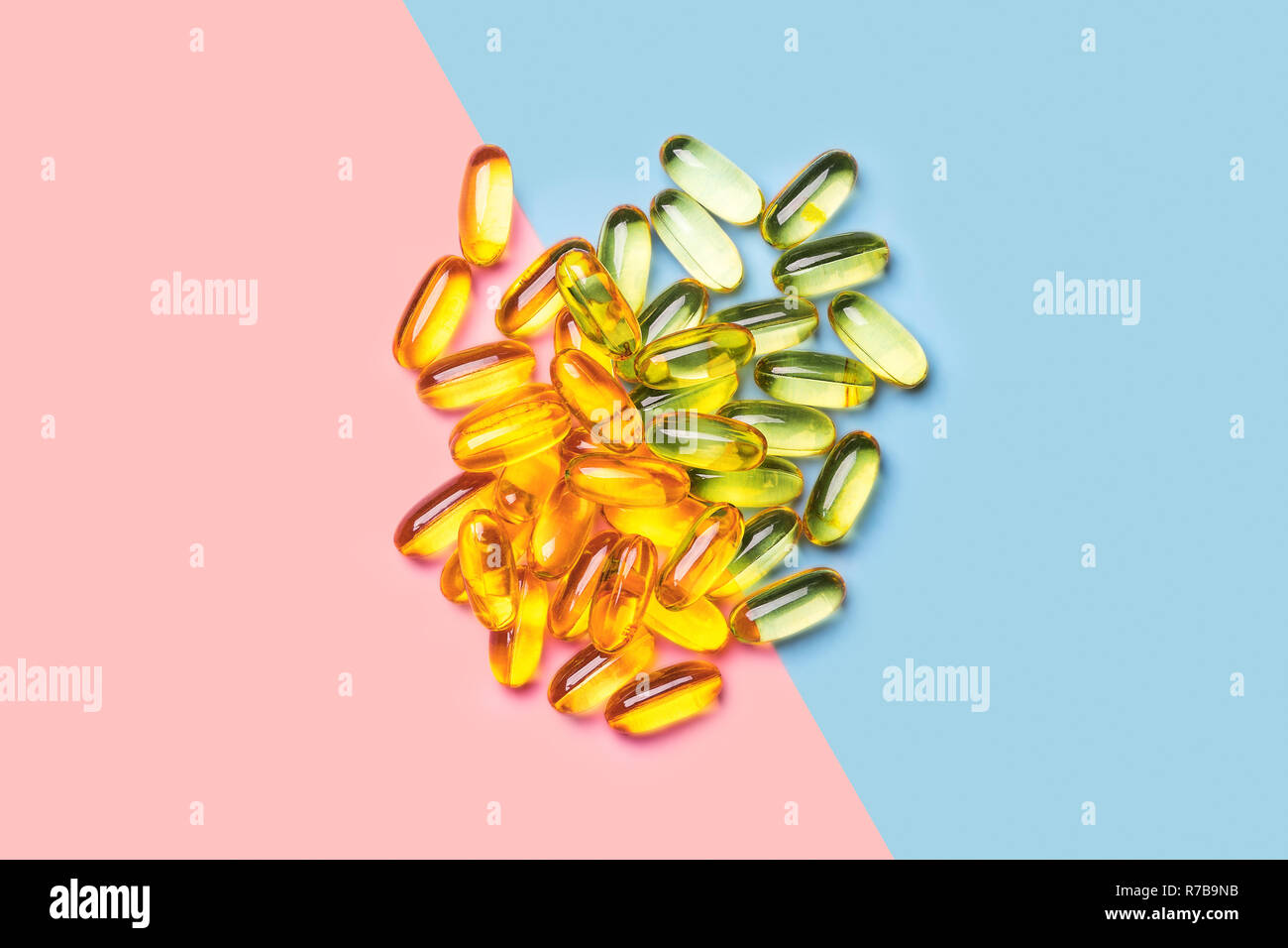 Un mucchio di colore giallo brillante olio di pesce capsule in rosa chiaro e sfondo blu shot con luce di studio Foto Stock