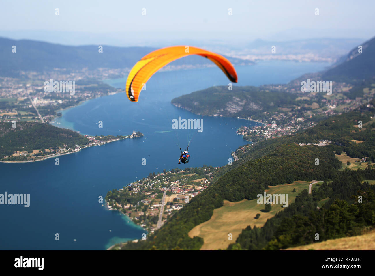 Un pilota di tandem e i suoi passeggeri battenti nella parte anteriore del Col de la Forclaz decollo con il lago di Annecy in background Foto Stock