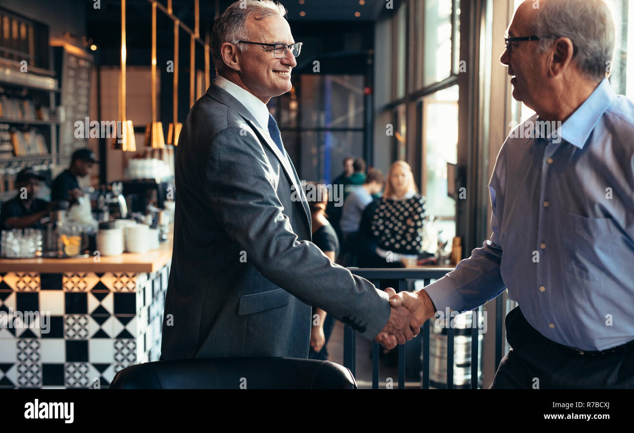 Uomo d'affari anziano che stringe la mano a un uomo al ristorante. uomini d'affari che si incontrano in un bar moderno con una stretta di mano. Foto Stock