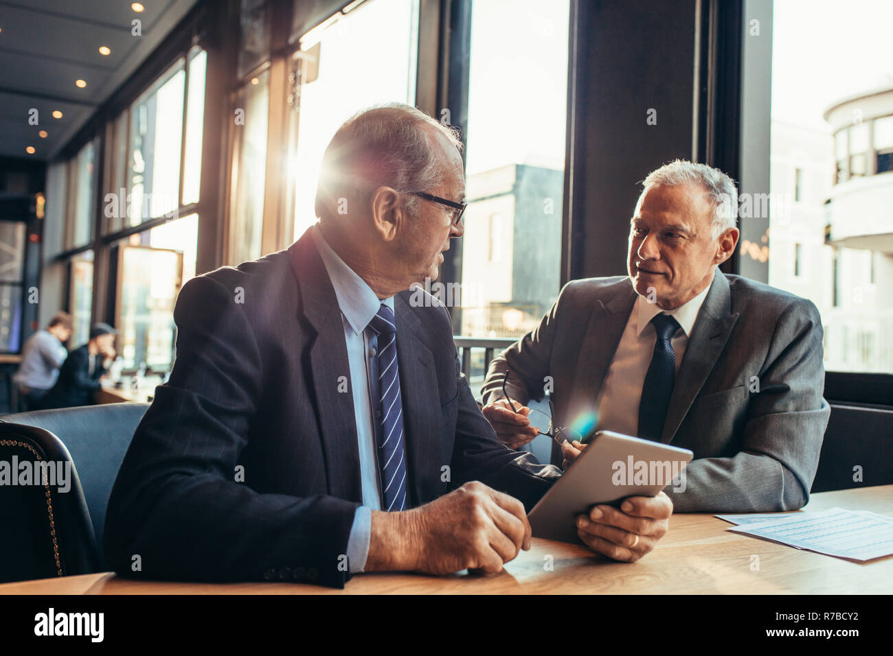 Uomo d'affari anziano che ascolta il suo partner al bar. uomo d'affari con un tablet digitale che parla con un collega durante una moderna riunione in un bar. Foto Stock