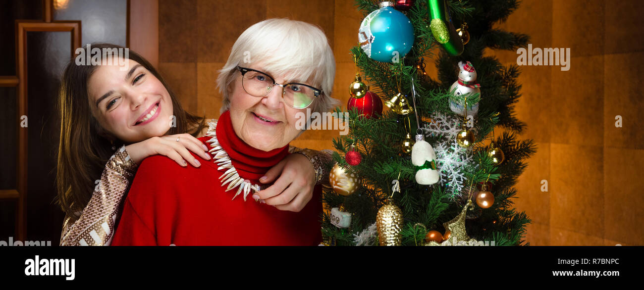 Nuovo anno. senior la nonna e la giovane donna caucasica, adolescente vicino a albero di natale. nipote, teen abbracciava, abbraccia la vecchia nonna. Felice compan Foto Stock