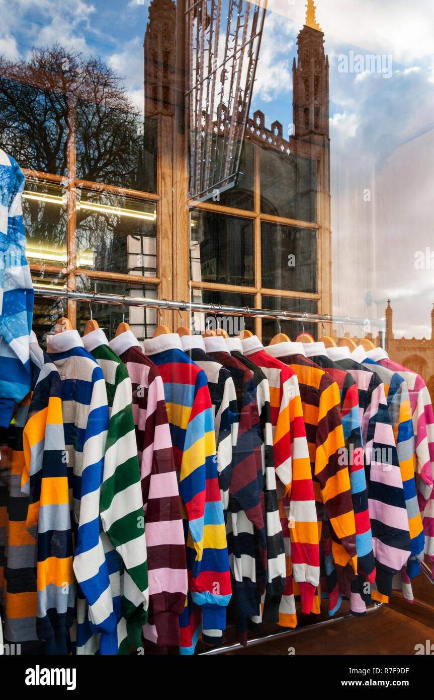 Colorate camicie rugby per la vendita in un negozio di Cambridge finestra con la riflessione della Cappella del King's College. Foto Stock