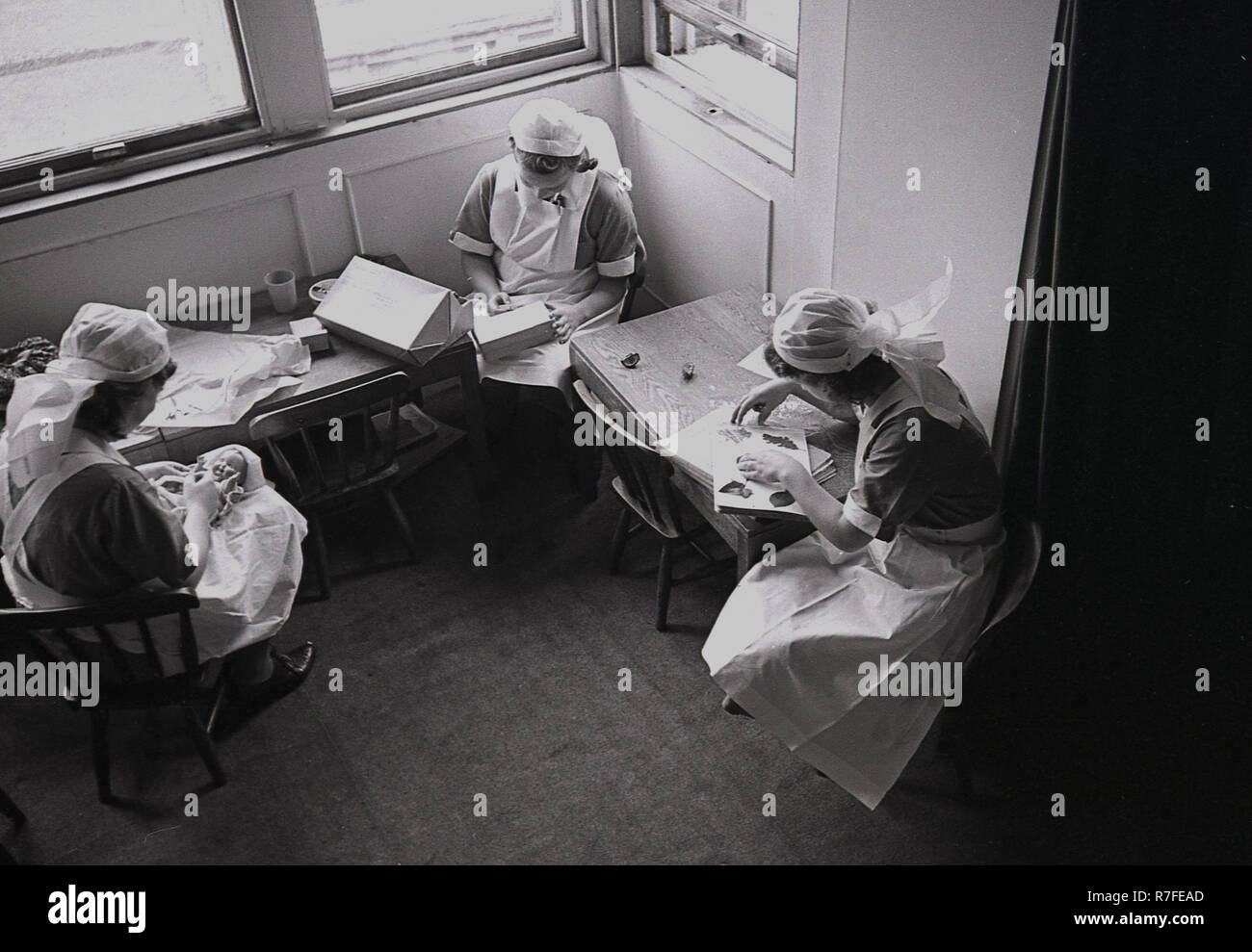 1940s, storico, WW2, il tempo di guerra e tre uniformata personale infermiere in una casa di campagna la preparazione di attività e giocattoli per il prossimo arrivo di evacuare bambini di città, Inghilterra, Regno Unito. Foto Stock