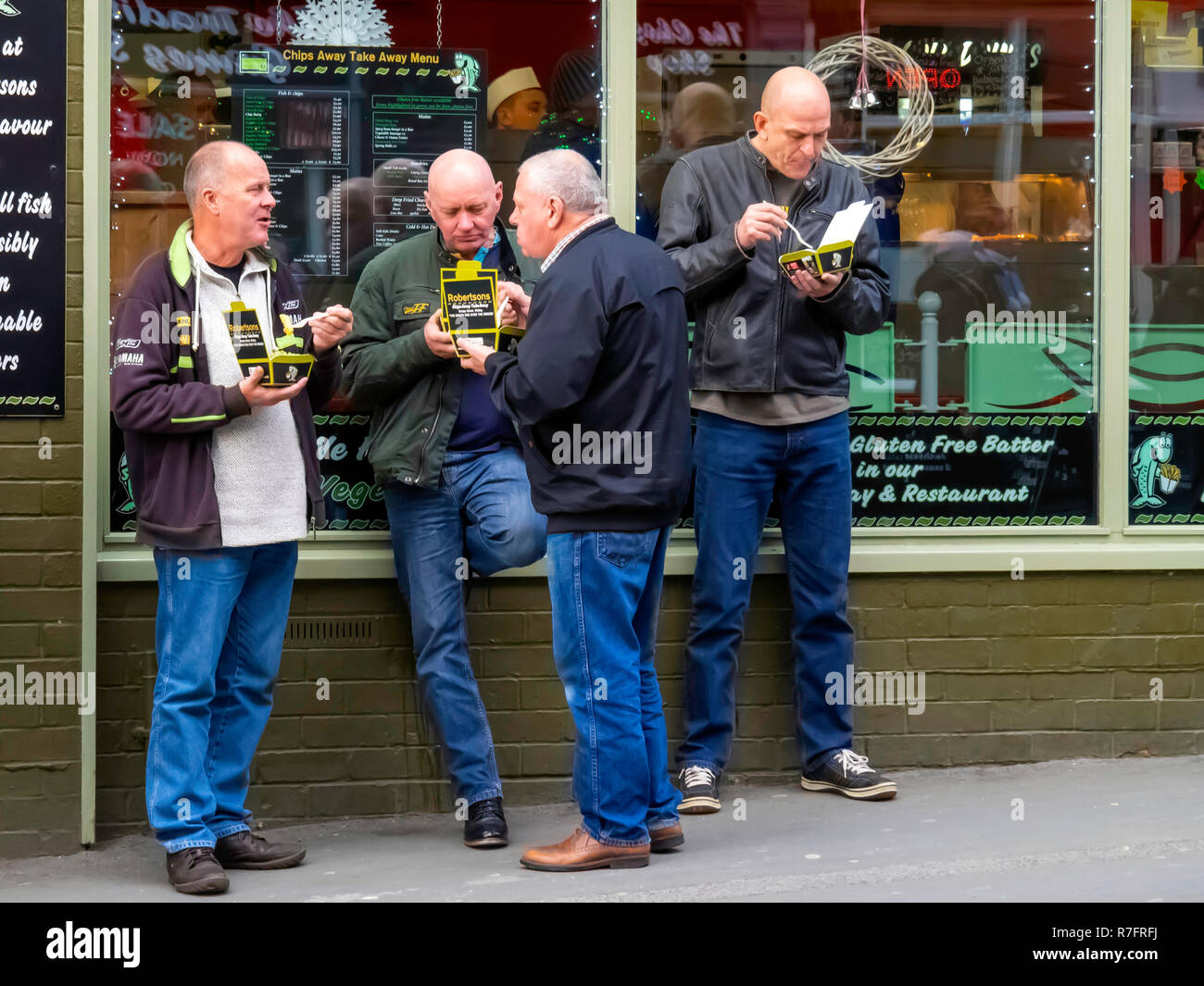Un gruppo di quattro persone di mezza età uomini bianchi, chiacchierando e gustando take-away pesce e patatine a Whitby North Yorkshire. Foto Stock