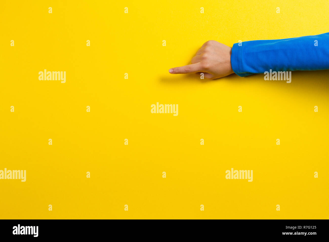Il capretto di puntamento a mano o toccando qualcosa su sfondo giallo Foto Stock