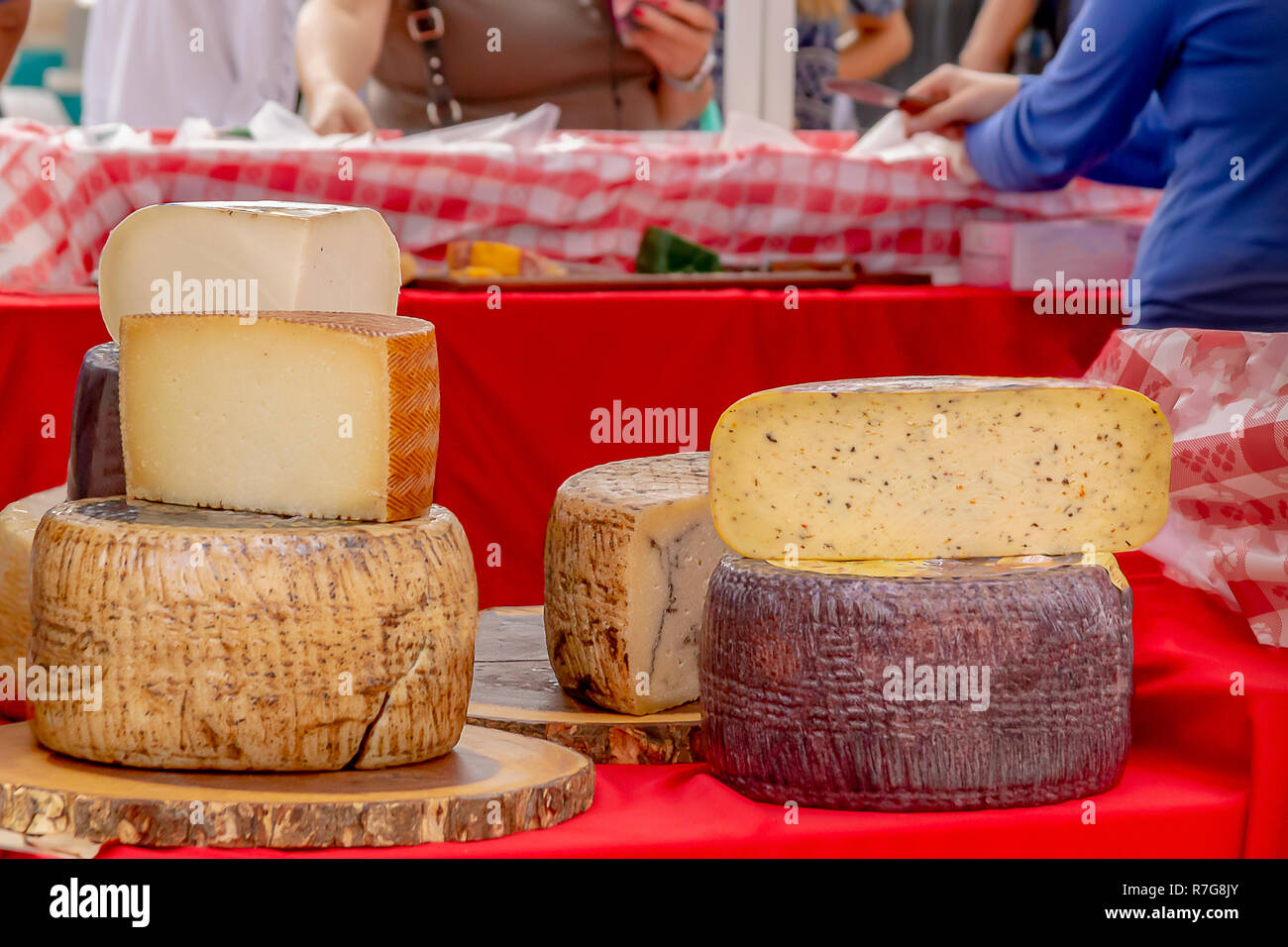 Impilate i turni di formaggio sono visualizzate in all'aperto il mercato degli agricoltori mentre la gente shop. Un formaggio server è consegnare campioni gratuiti di formaggio. Foto Stock