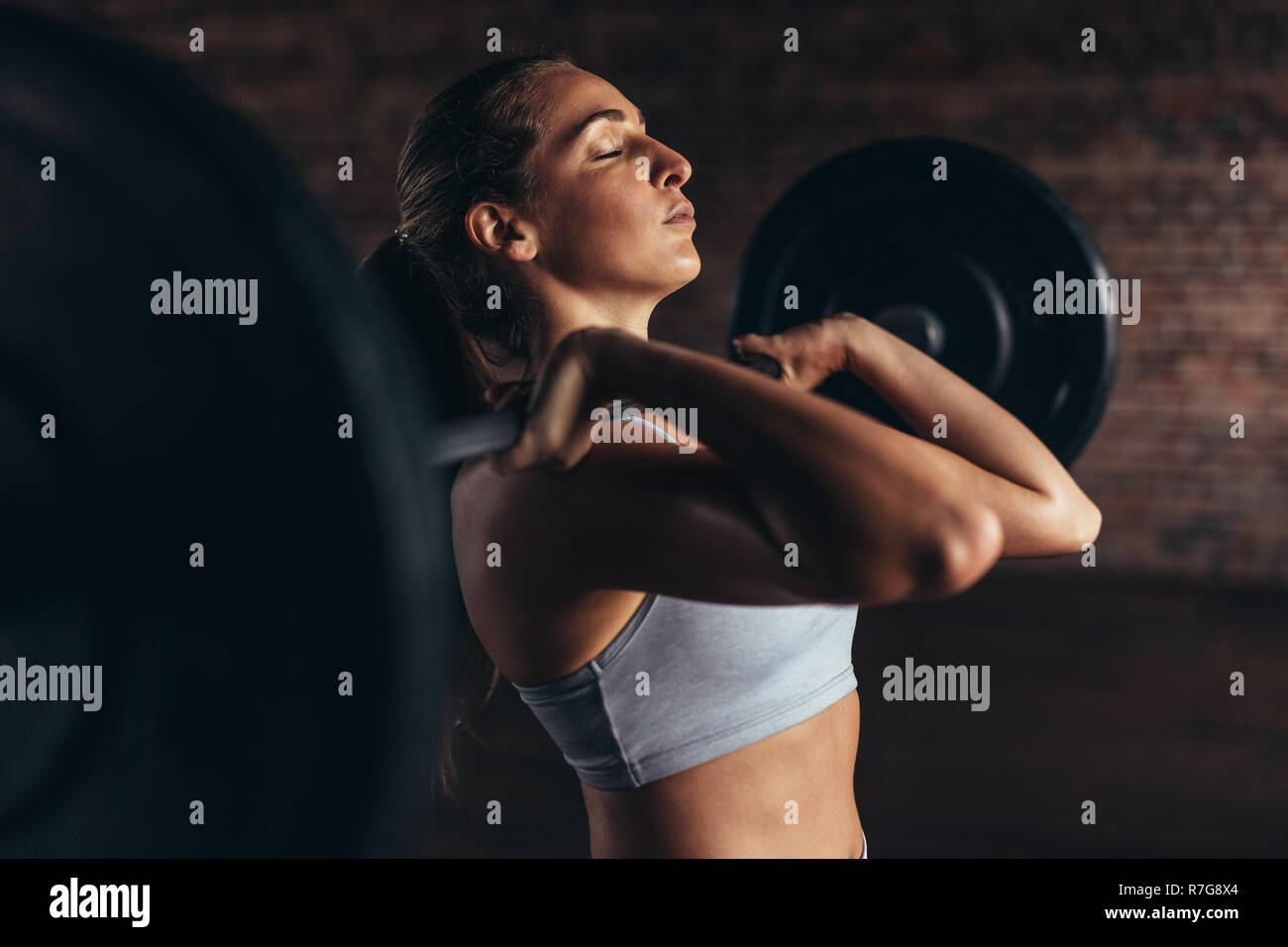 Giovane donna esercizio utilizzando barbell con pesi pesanti in un fitness club. Femmina in sportswear fare sollevamento pesi nella palestra. Foto Stock