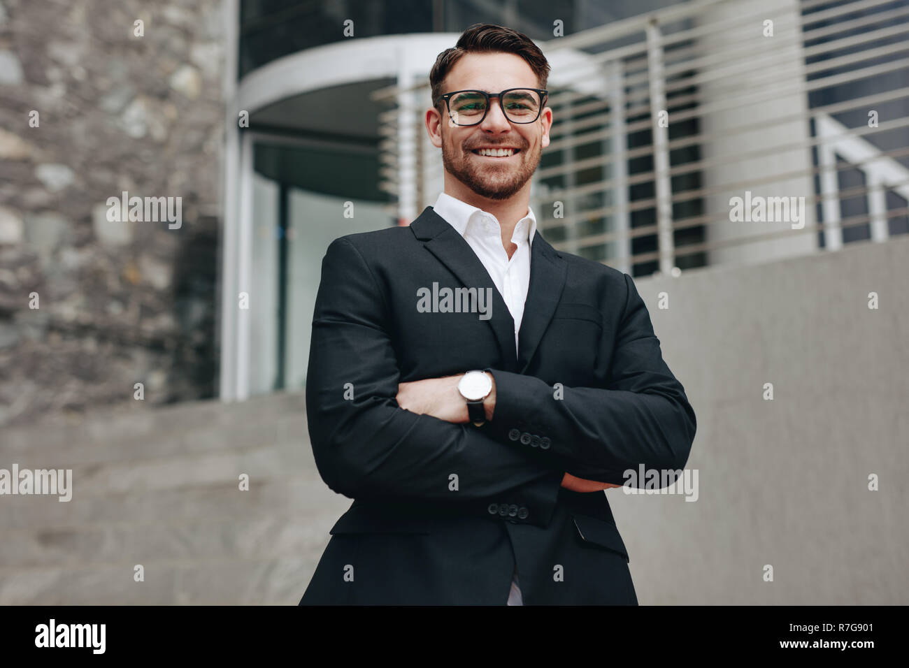 Sorridente imprenditore all'aperto in piedi con le braccia incrociate. Uomo in abiti formali in piedi al di fuori di un edificio con bracci ripiegati. Foto Stock