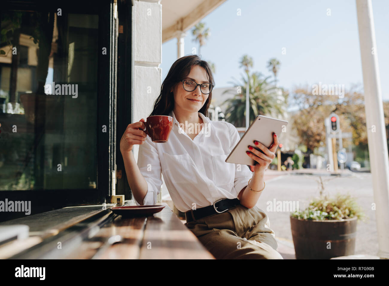 donna d'affari seduta in un bar con una tazza di caffè e un tablet digitale. Donna seduta al bancone del bar con un tablet digitale che beve un caffè. Foto Stock