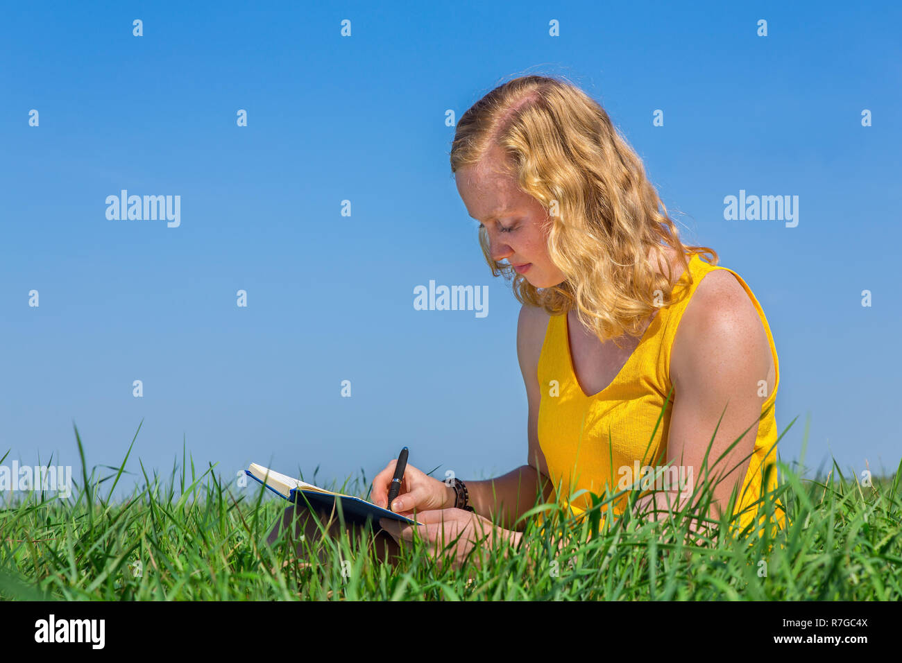 Giovane donna caucasica iscritto in erba con cielo blu Foto Stock