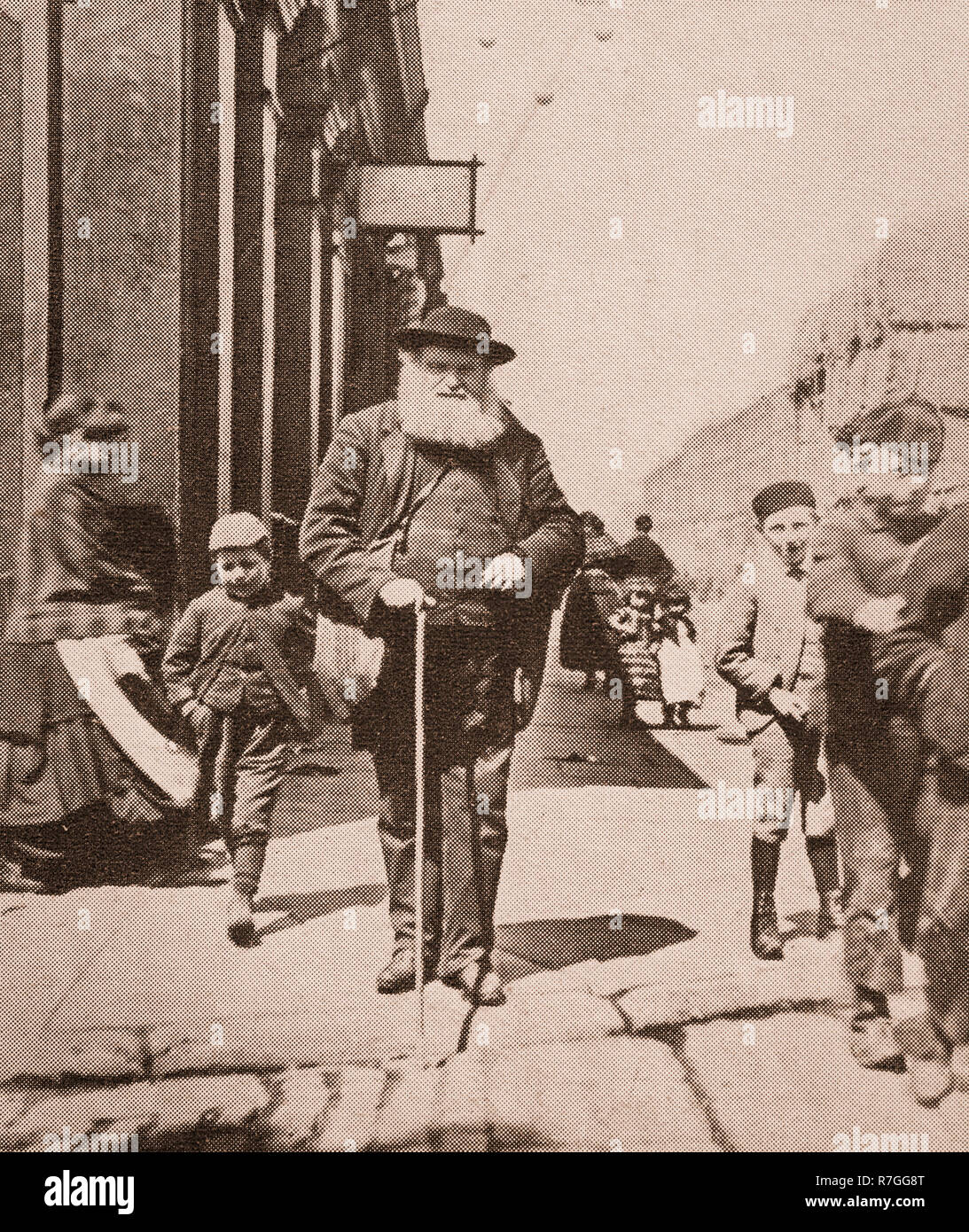 La vita per la lavorazione di folk in stile vittoriano giorni... Un uomo cieco con il suo bastone bianco e un entourage di kids in grande Omero Street, Liverpool, Merseyside England Foto Stock