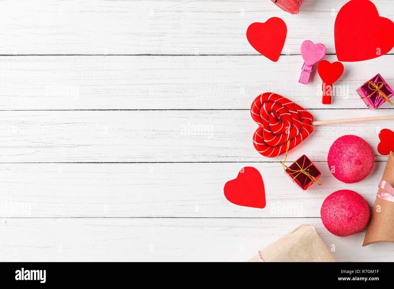 Il giorno di San Valentino decorazioni con lecca-lecca a forma di cuore, confezioni regalo e caramelle sul bianco sullo sfondo di legno con copia spazio, vista dall'alto Foto Stock