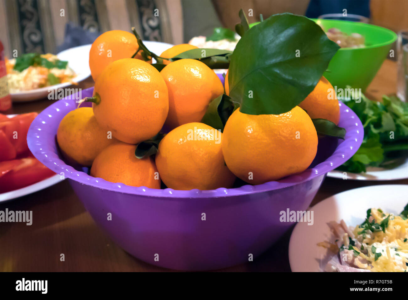 Succosa mature tangerini freschi con foglia verde in un viola coppa in plastica su un rustico tavolo di partito Foto Stock