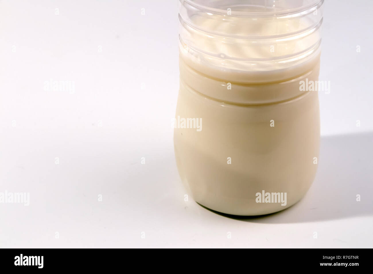 Fondo della plastica trasparente bottiglia piena a metà di latte isolato su bianco Foto Stock