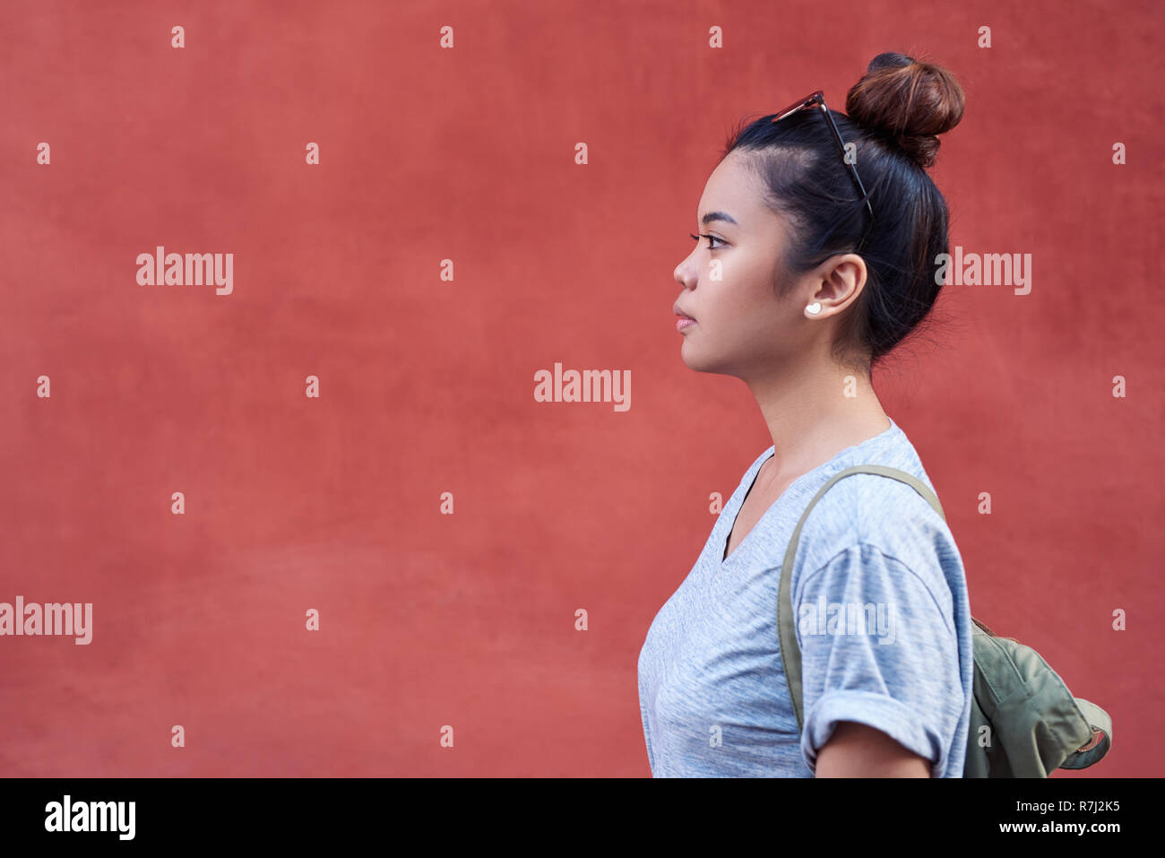 Giovane donna asiatica lateralmente in piedi di fronte a una parete Foto Stock