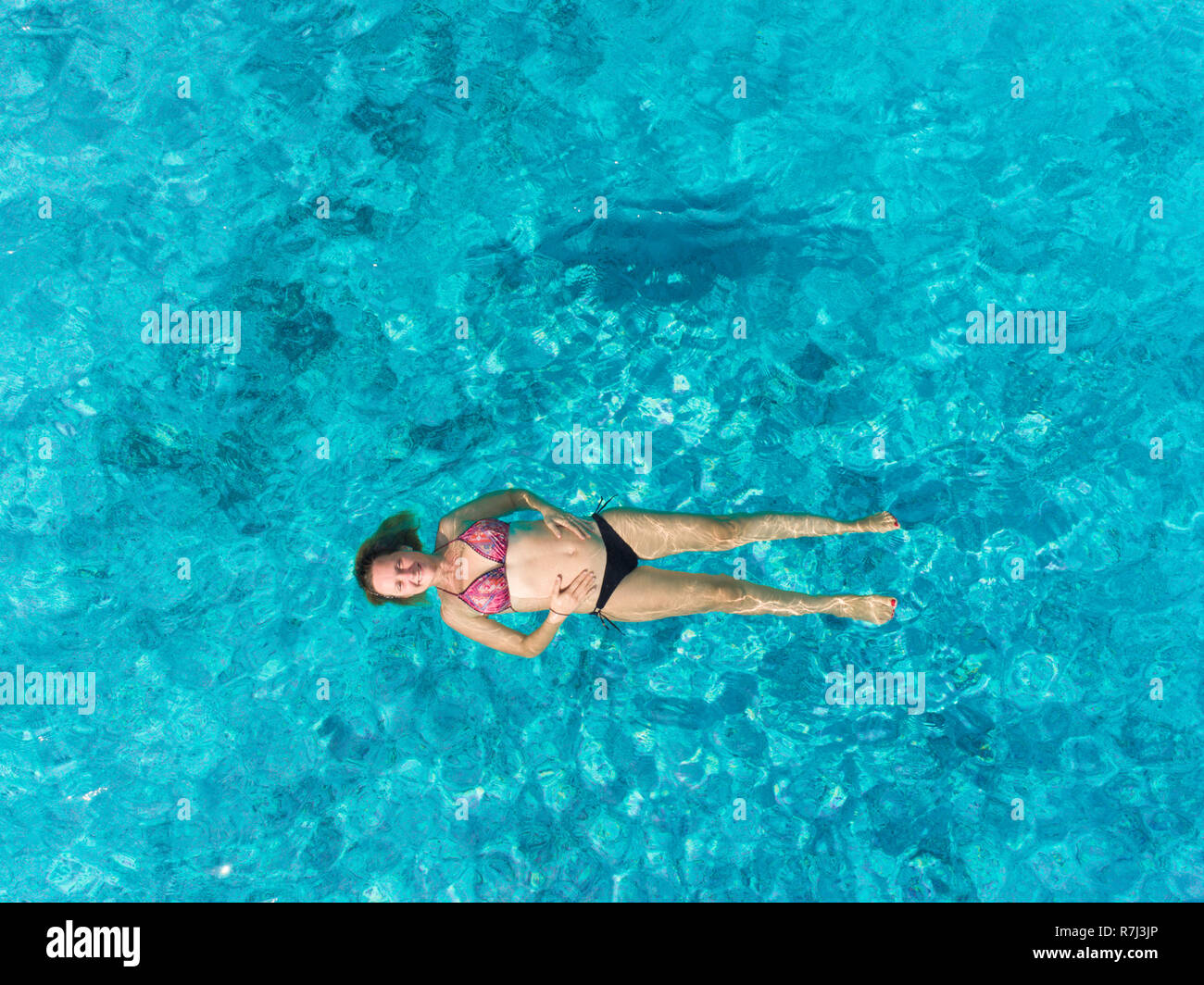 Vista aerea della donna incinta galleggiante sulla sua schiena in mare trasparente mentre tiene il suo pancino. Foto Stock