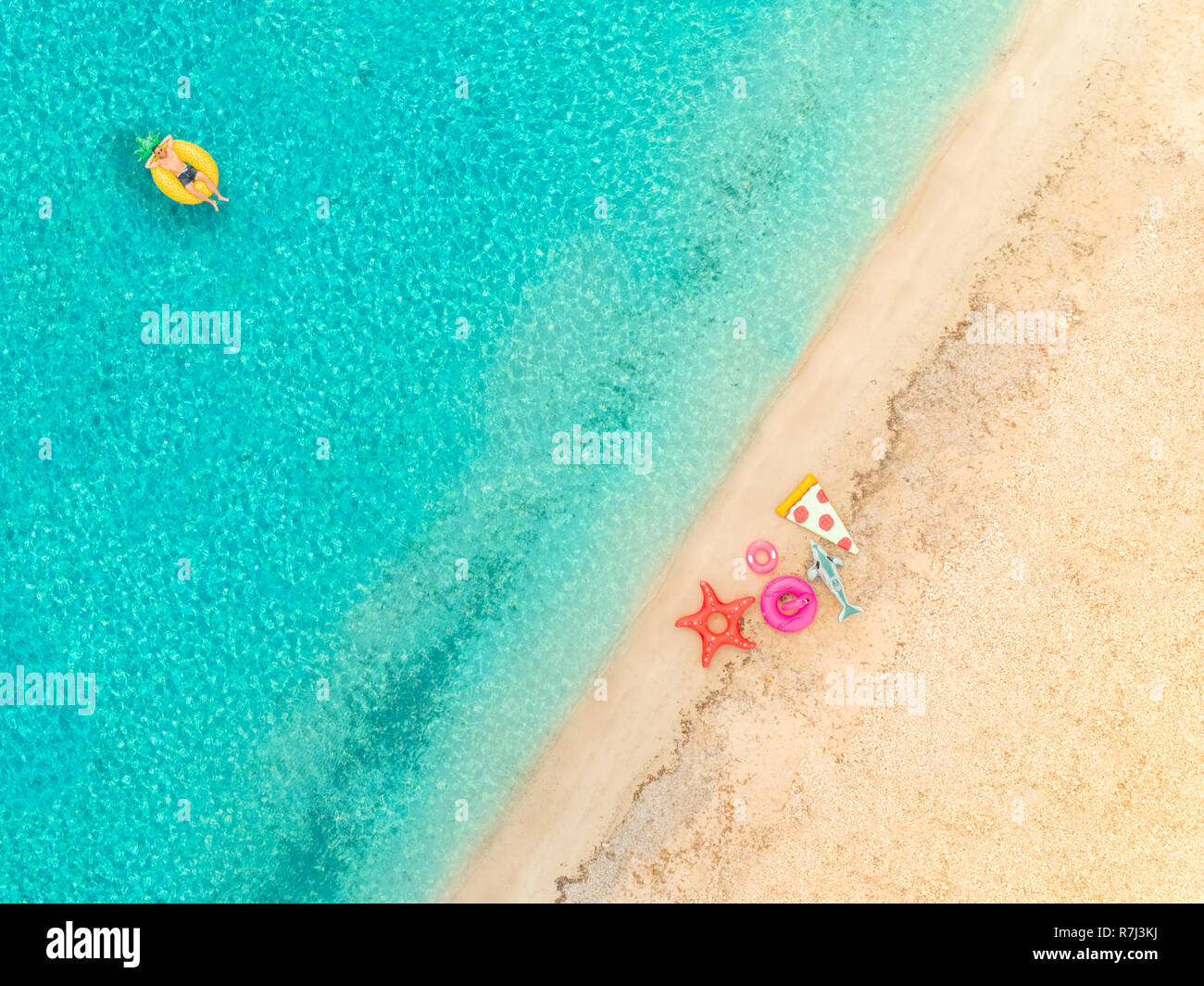 Vista aerea dell'uomo sul galleggiante gonfiabile materasso ananas dalla spiaggia sabbiosa e anelli gonfiabile. Foto Stock