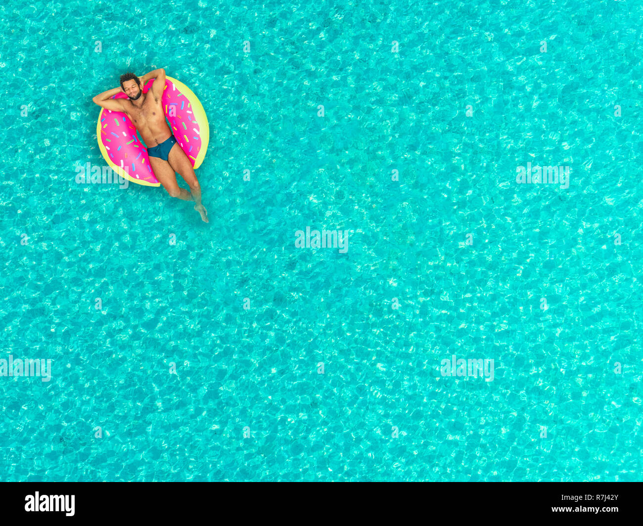 Vista aerea dell'uomo galleggiante sulla ciambella gonfiabile materasso, rilassante e sorridente. Foto Stock
