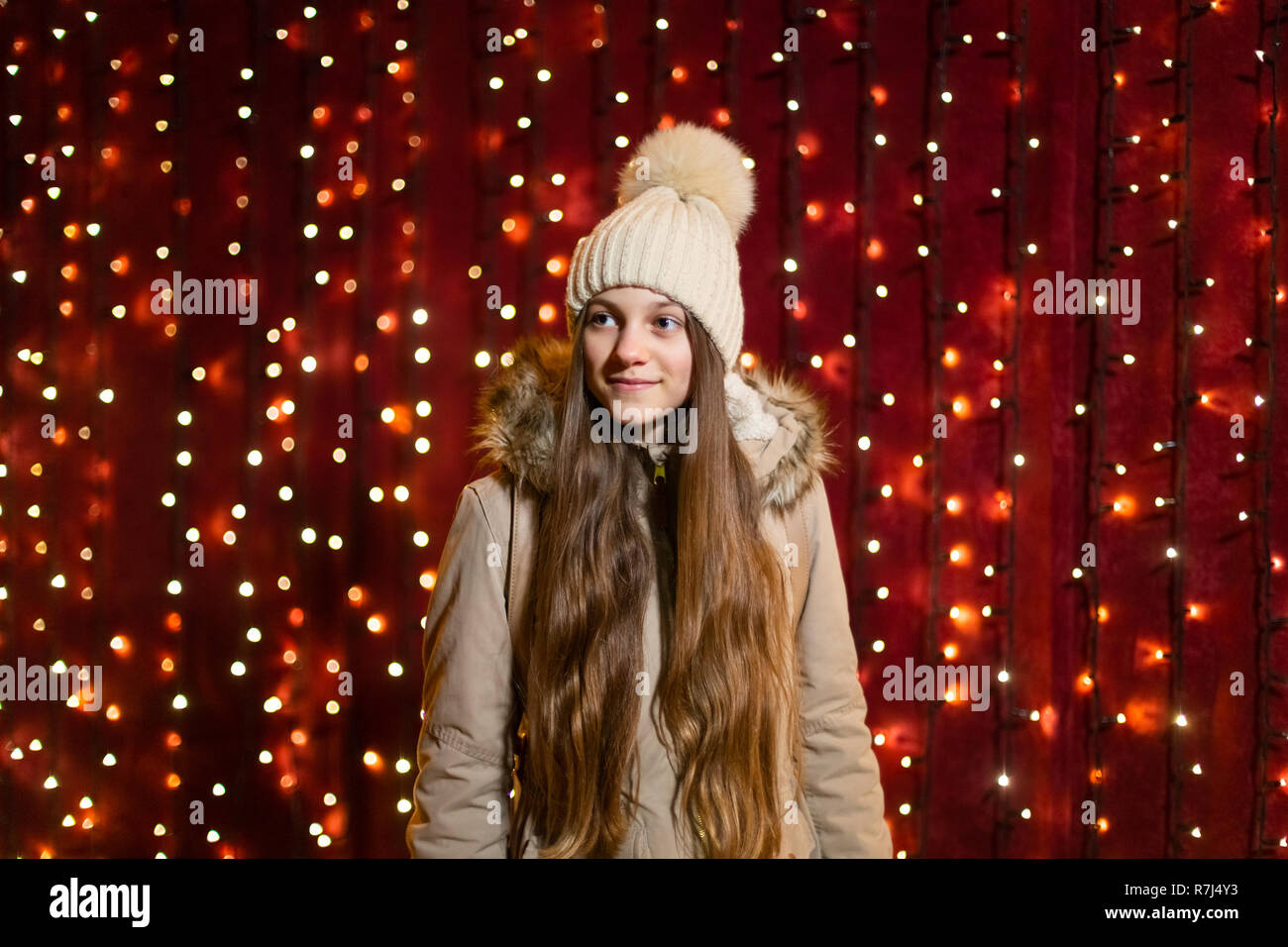Adolescente con capelli lunghi in posa nella parte anteriore della parete di luci al mercato di Natale. Foto Stock