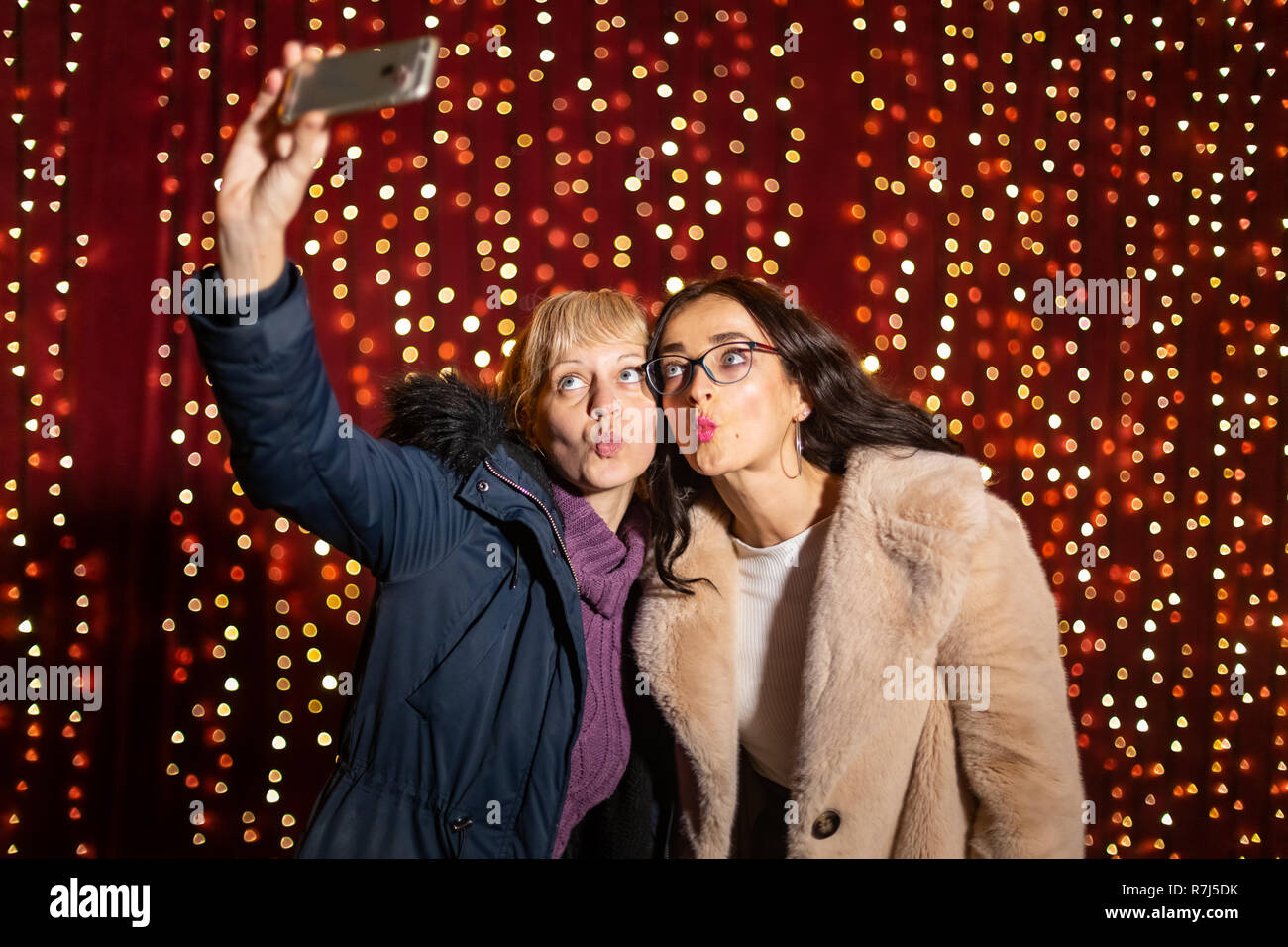 Due donne attraenti tenendo selfie nella parte anteriore della parete di luce al mercato di Natale. Foto Stock