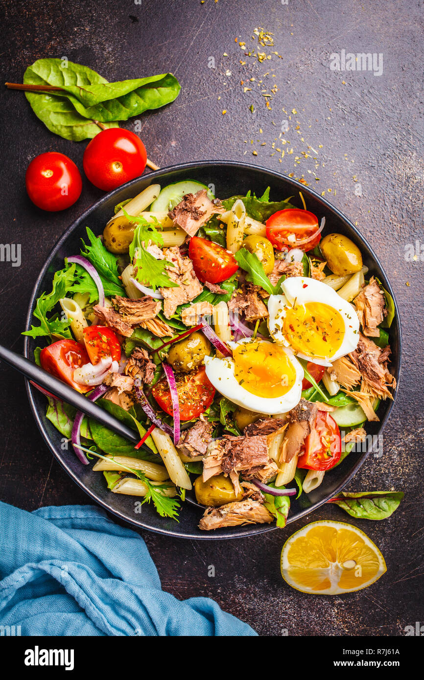 Insalata di tonno con la pasta di olive, ortaggi e Uovo affogato in una piastra nera su sfondo scuro, vista dall'alto. Foto Stock