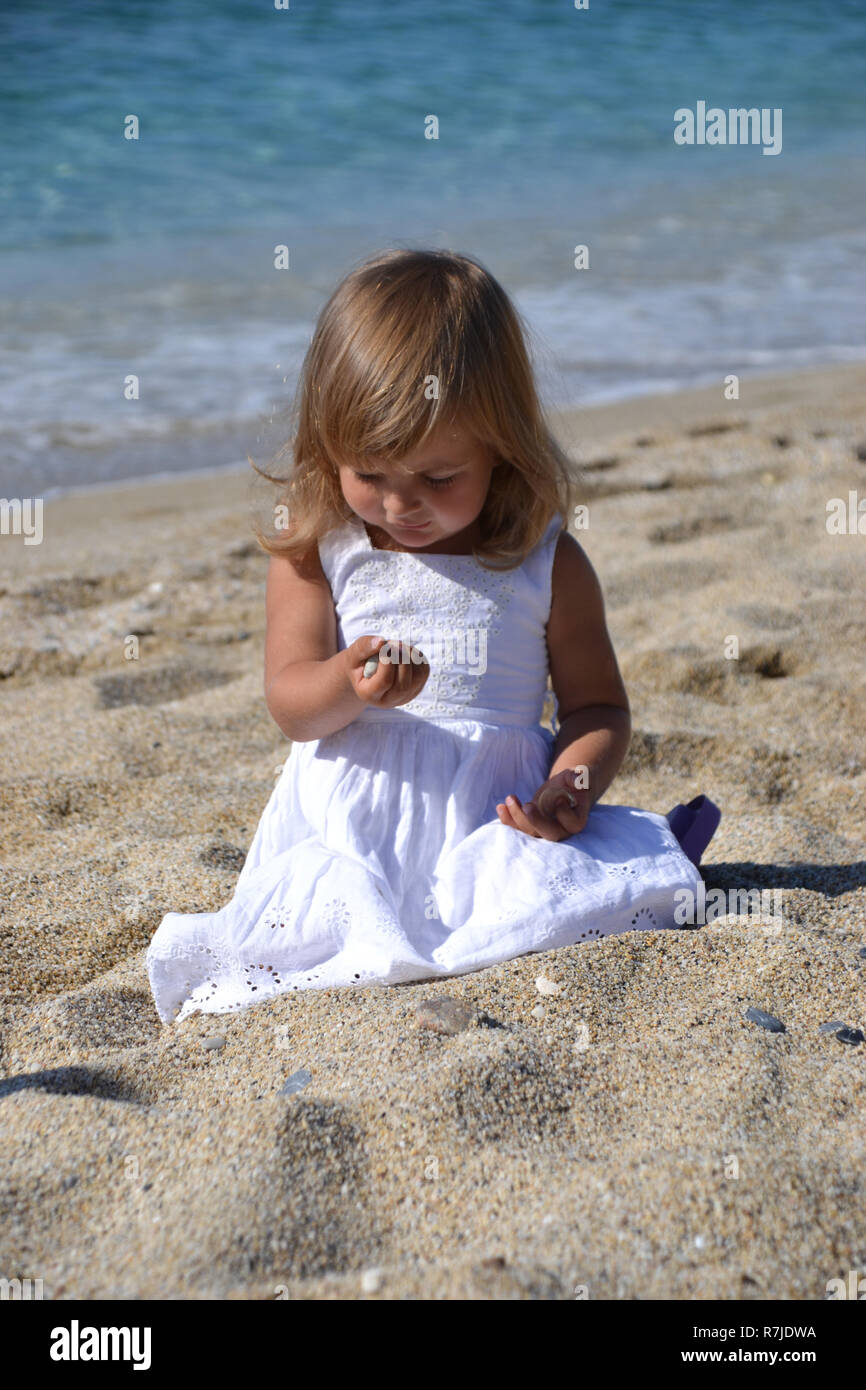 Bambina gioca con un ciottolo sulla spiaggia, mare in background Foto Stock