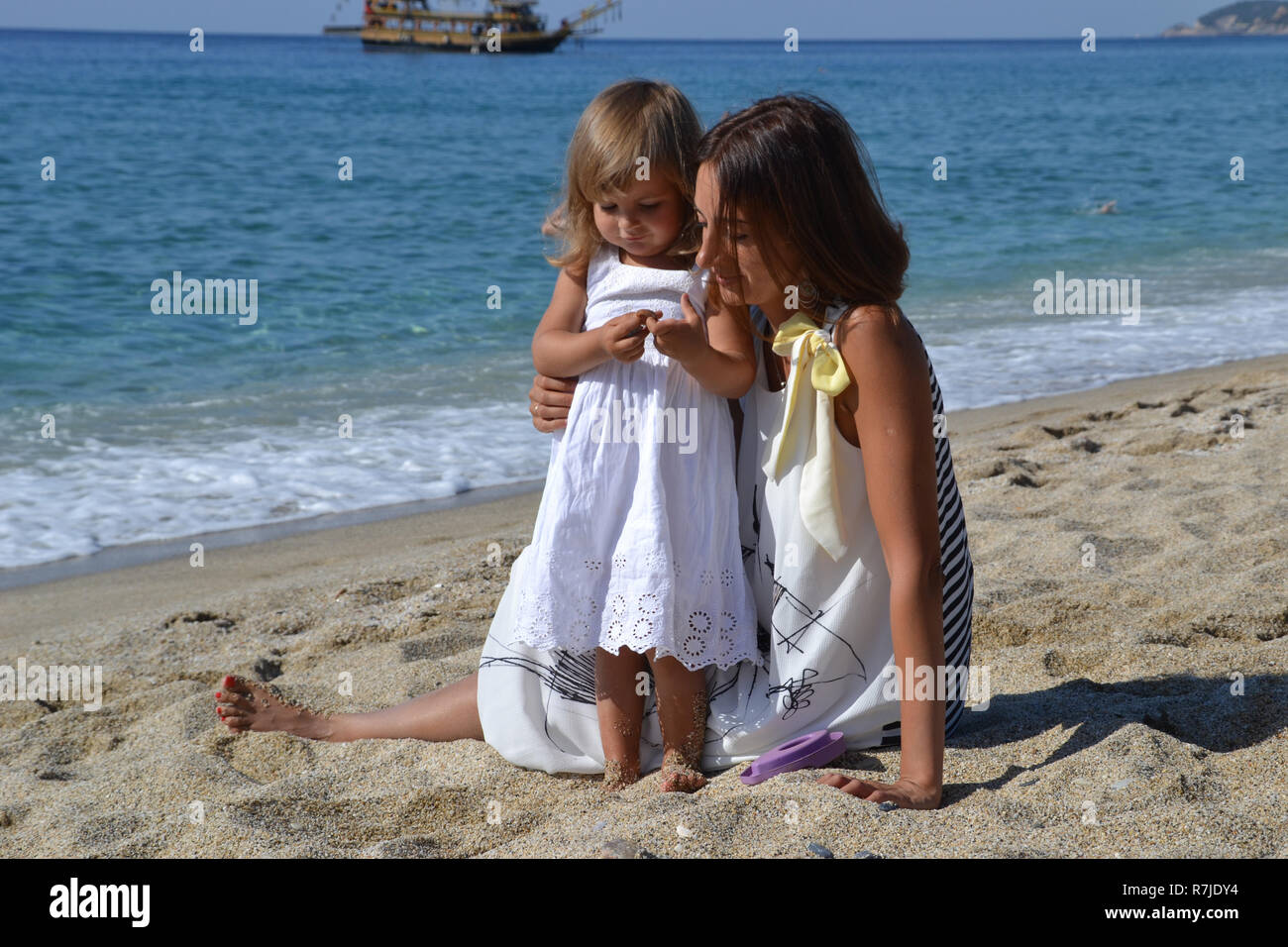 La mamma e la sua piccola ragazza ragazzo giocando insieme a conchiglia sulla spiaggia, la felicità della famiglia vicino al mare Foto Stock