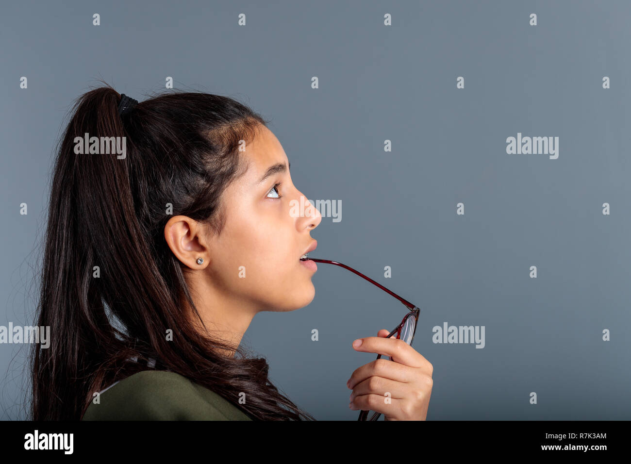 Ragazza adolescente meditando con occhiali maniglia in bocca, vista di profilo di bruna cercando nello spazio Foto Stock
