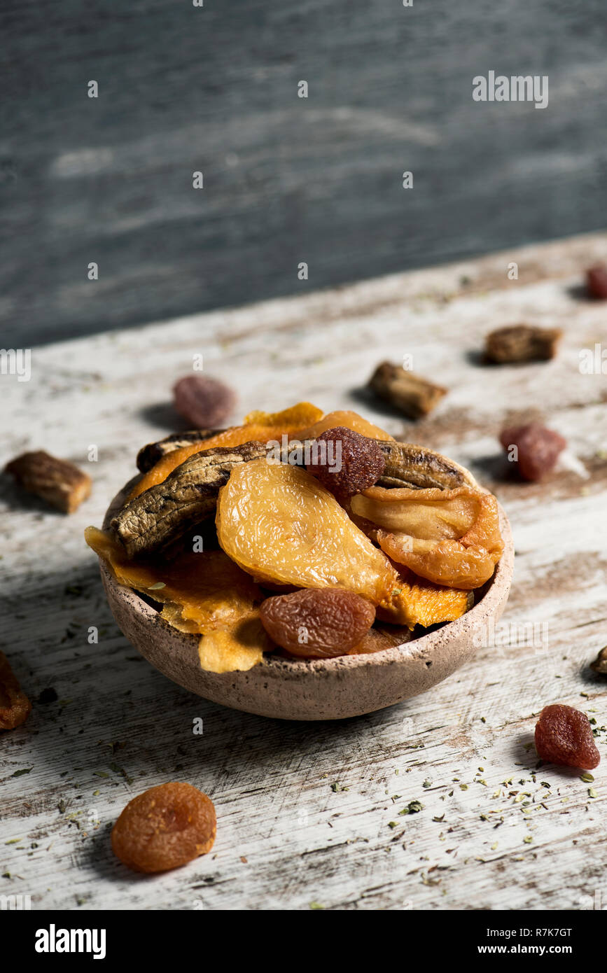 Primo piano di un rustico vaso di terracotta pieno di assortimento di frutta secca, come pera, pesca, banana, fragola, Apple o di albicocca, su di un tavolo di legno Foto Stock