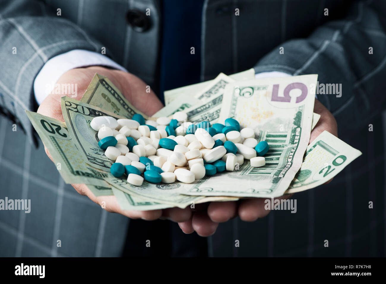 Primo piano di un giovane imprenditore caucasico, indossando un elegante abito grigio, con una pila di fatture del dollaro e pillole di diversi colori nelle sue mani Foto Stock