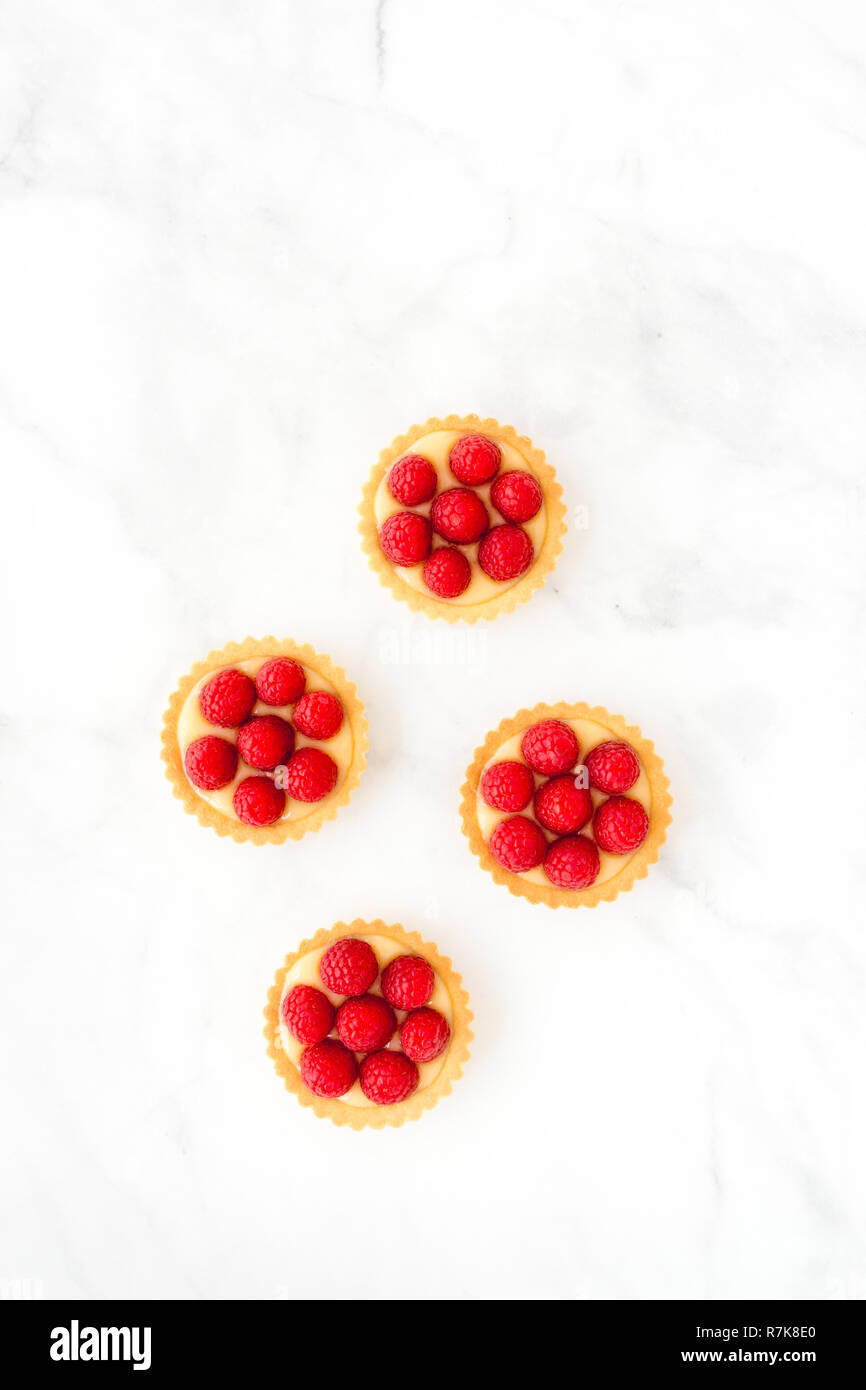 Lampone mini torte, pasticcini, con crema di limone su marmo bianco sfondo con copia spazio. Vista dall'alto. Foto Stock