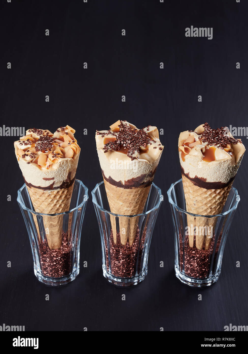 Tre caramello coni gelato, impostato in bicchieri riempiti con cristalli di zucchero, su scuro dello sfondo marrone Foto Stock