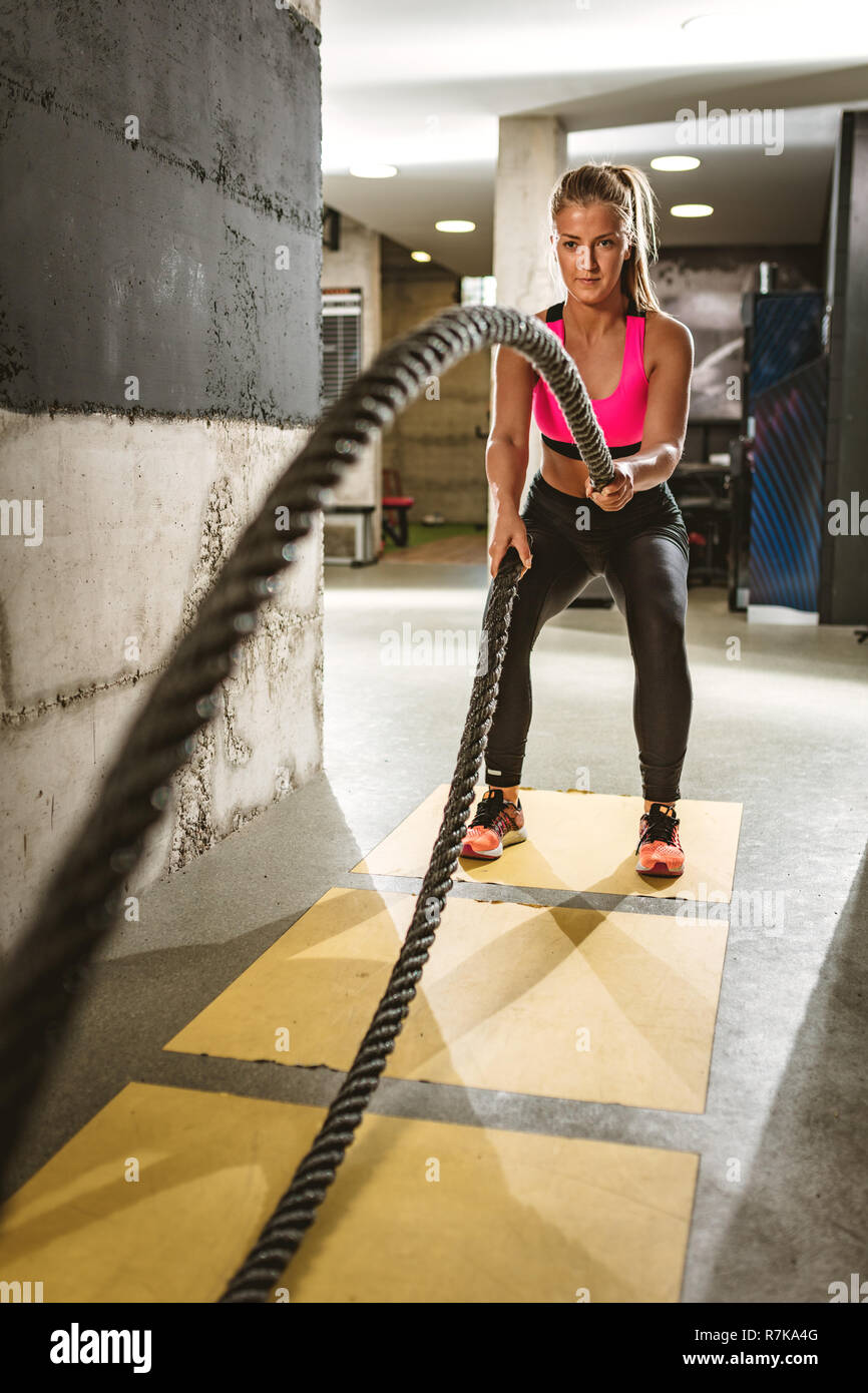 Giovane donna facendo forza di formazione utilizzando corde pesanti in palestra. Atleta muovendo le corde in moto ondoso come parte della forza di formazione. Foto Stock