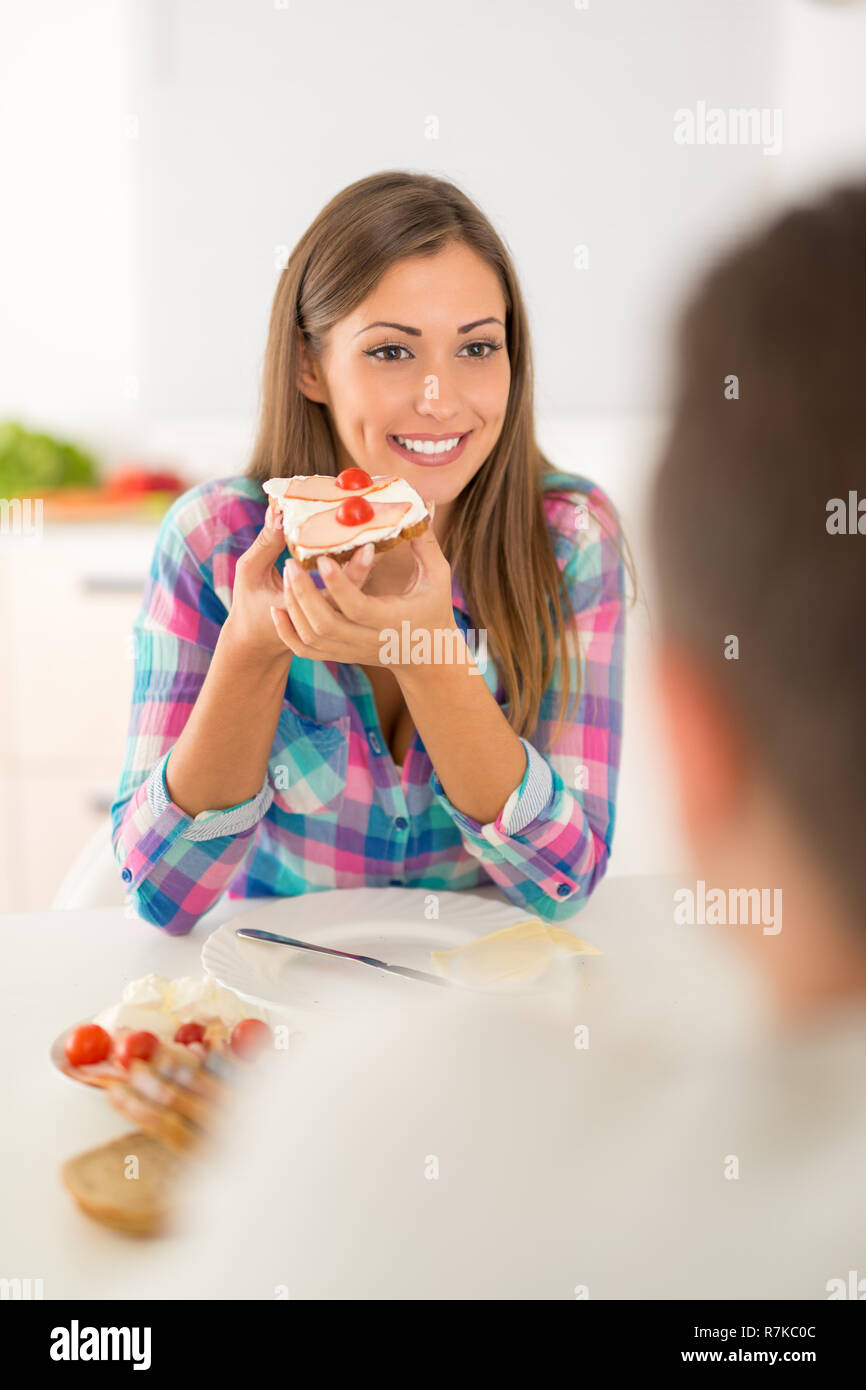 Bella coppia Giovane avente la colazione nella cucina domestica. Ragazza mangiare panino e cercando il suo fidanzato. Foto Stock