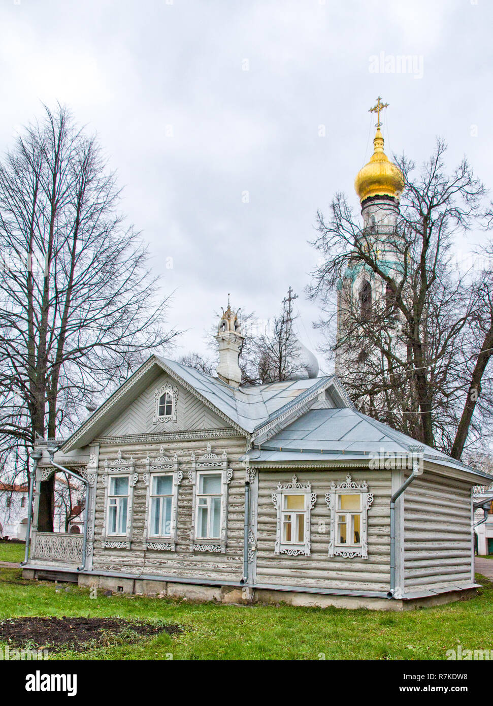 Vecchia casa in legno su un prato verde scolpito con windows. Chiesa in background. Il russo vecchia casa izba. Foto Stock