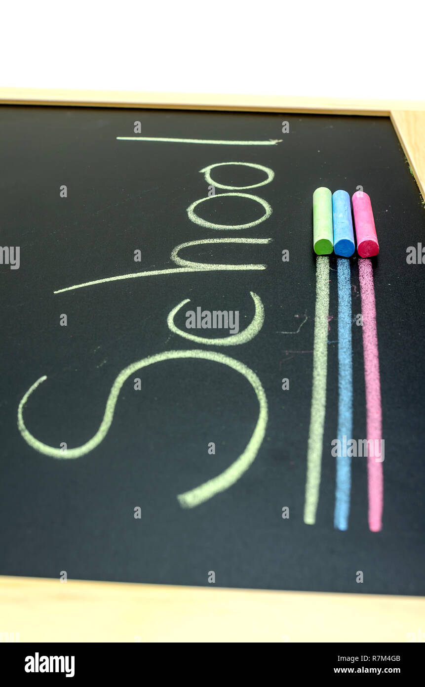 Dettaglio della scuola di parola scritta sulla lavagna con tre gessi colore giacente su di esso. Foto Stock