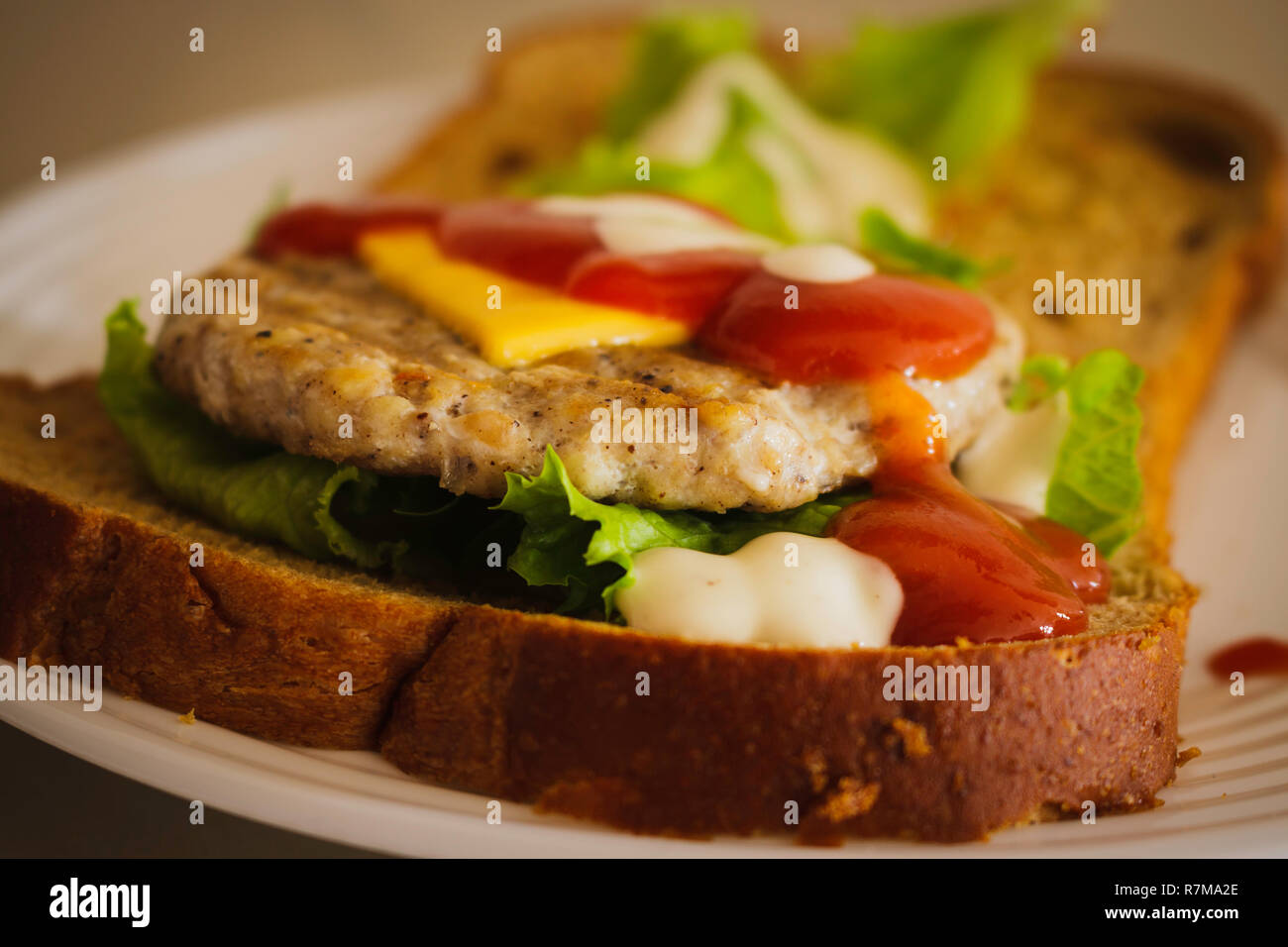 Hamburger fatto da grano integrale a fette di pane, formaggio, lattuga e condito con ketchup e condimento per insalata Foto Stock
