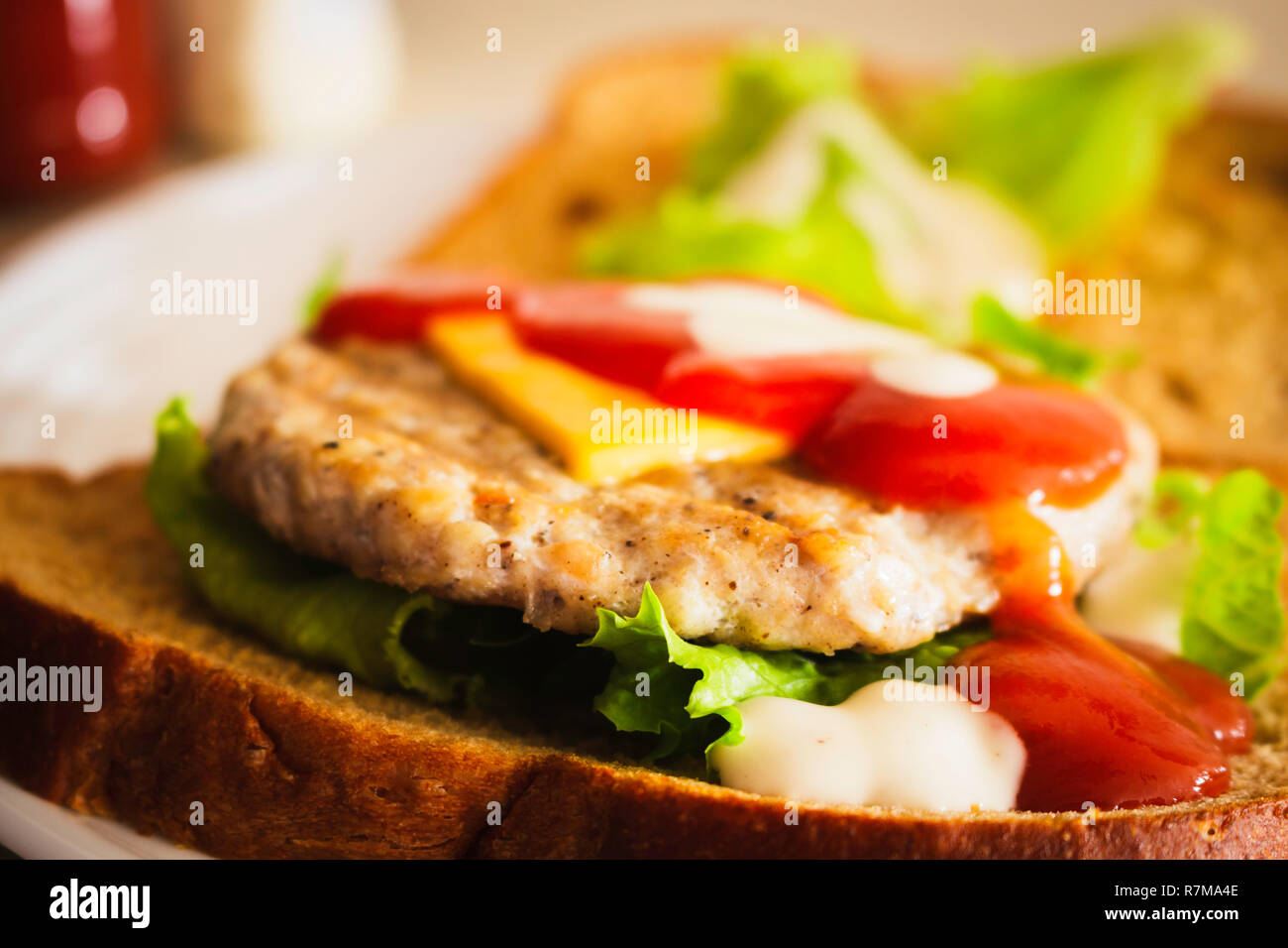 Hamburger fatto da grano integrale a fette di pane, formaggio, lattuga e condito con ketchup e condimento per insalata Foto Stock