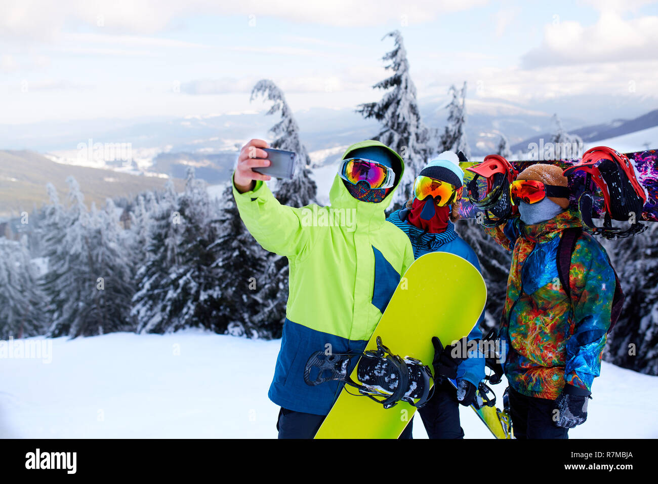Tre gli snowboarder tenendo selfie con la fotocamera dello smartphone a ski  resort. Gli amici di fotografare per la condivisione della rete sociale con  gli snowboard vicino alla foresta di indossare gli